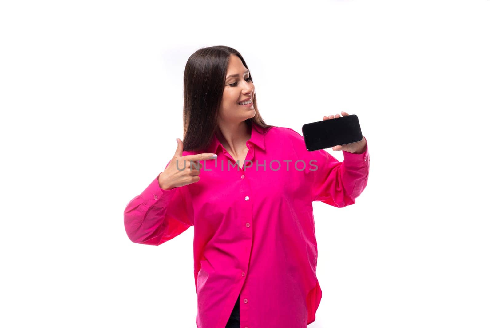 portrait of a cheerful european young lady with black hair in a crimson shirt with a smartphone in her hand.