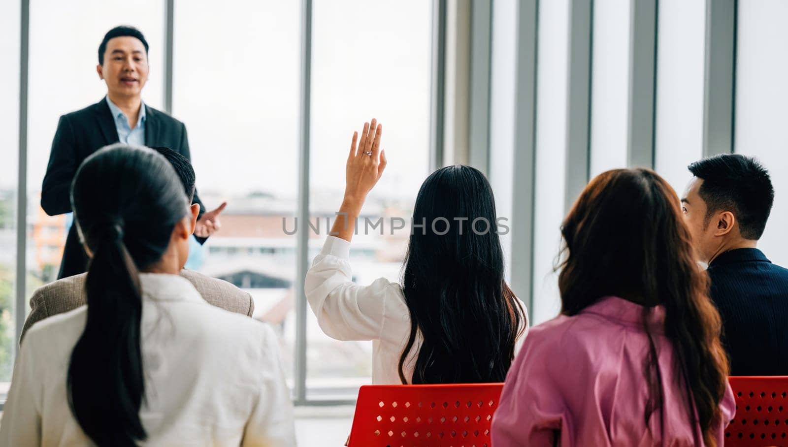 Diverse group of business professionals in seminar meeting room raises their hands reflecting active audience participation and strong sense of teamwork. It's all about question and answer concept. by Sorapop