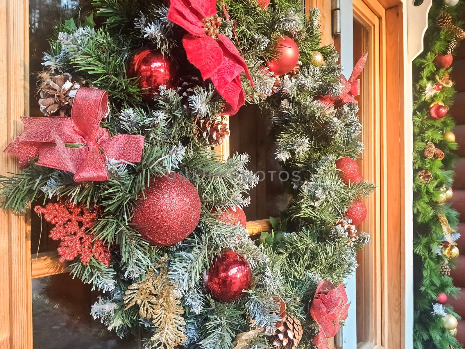 Christmas wreath with red and gold bauble decorations, bow, holly, mistletoe, pine cones and blue spruce fir over dark wood front door background.