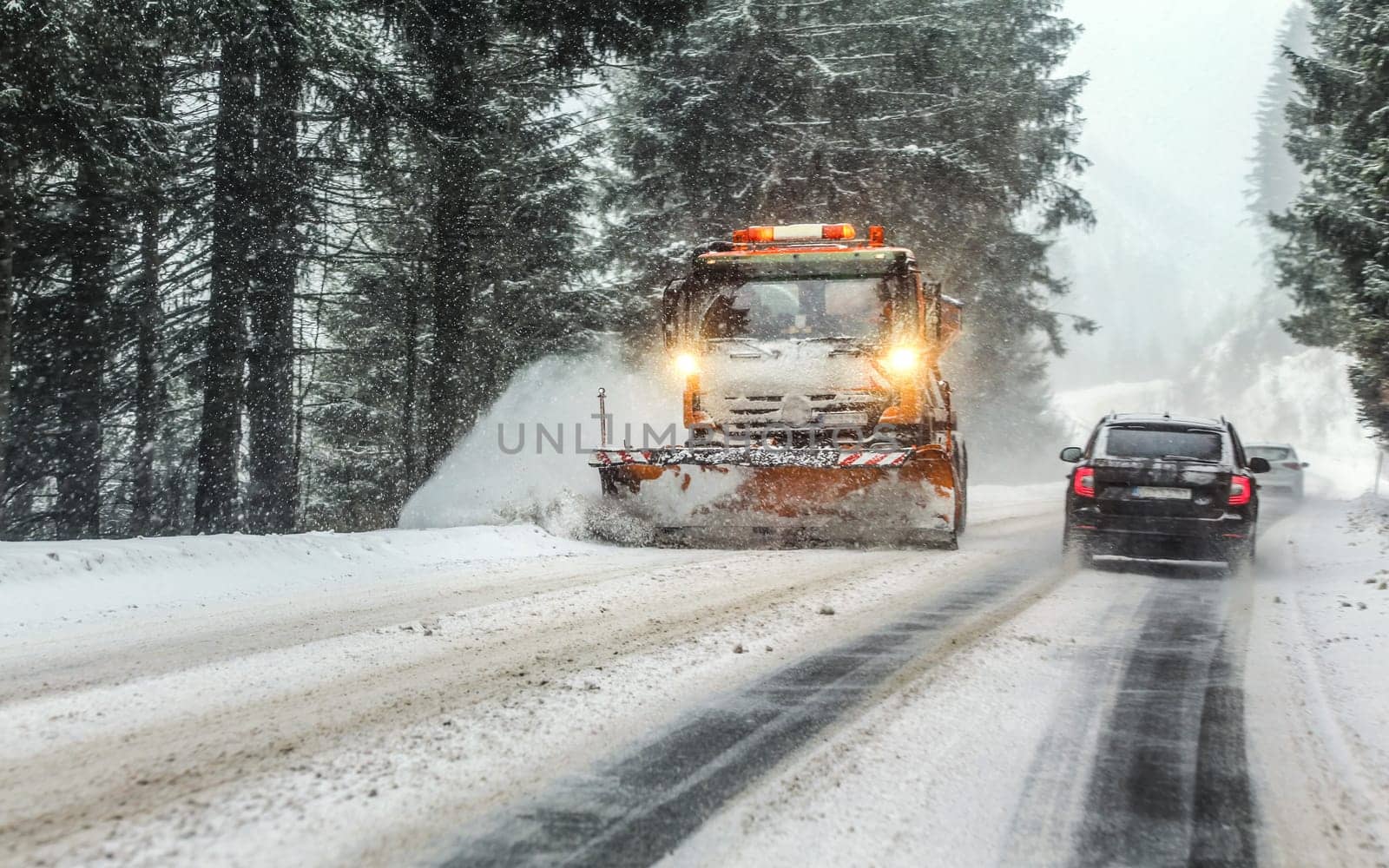 Liptovsky Hradok, Slovakia - January 08, 2019: Orange maintenance plough truck on forest road in snowstorm blizzard. Roads in this area get dangerous during winter.