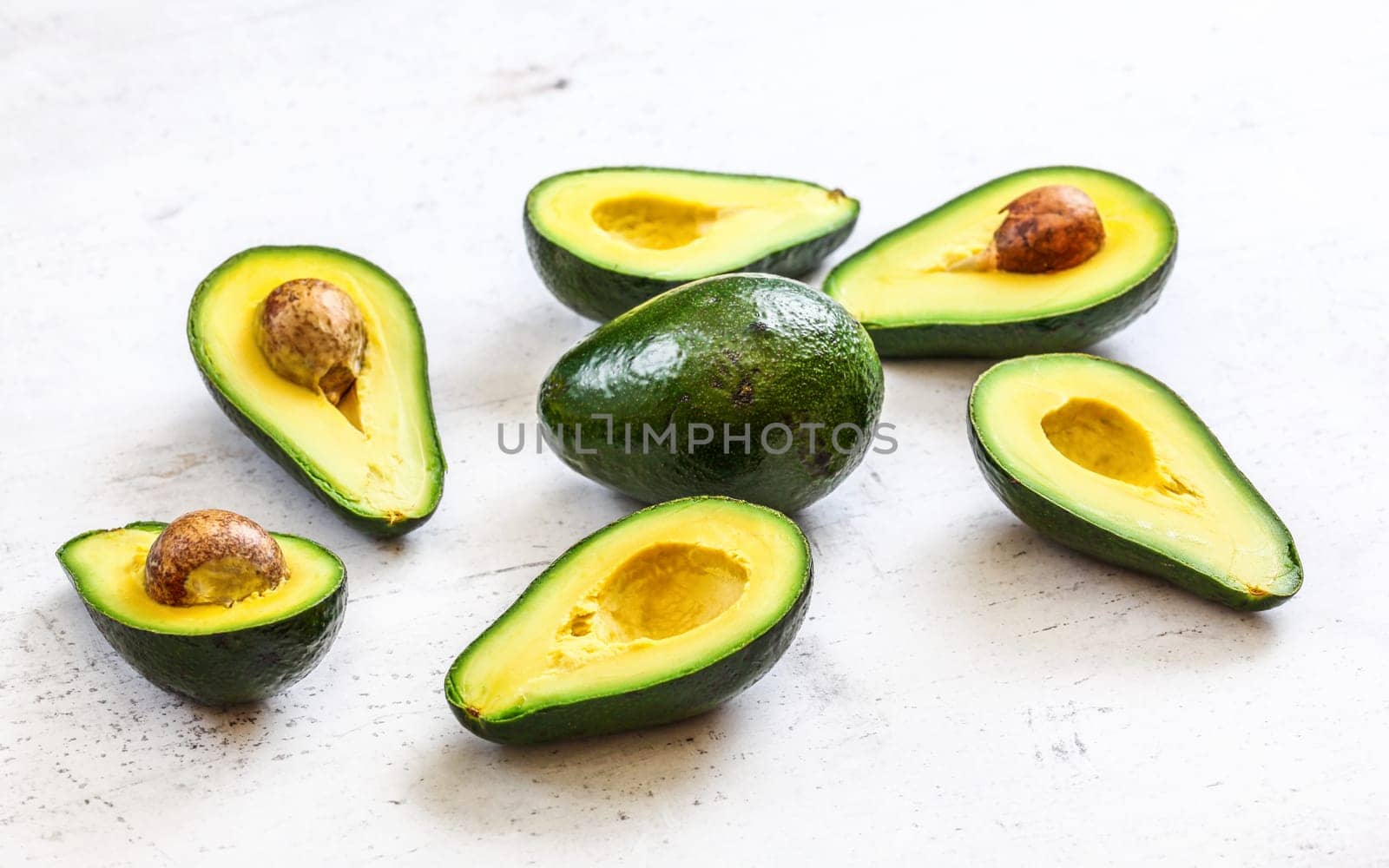 Avocados cut in half, one whole pear in middle, on white working board.