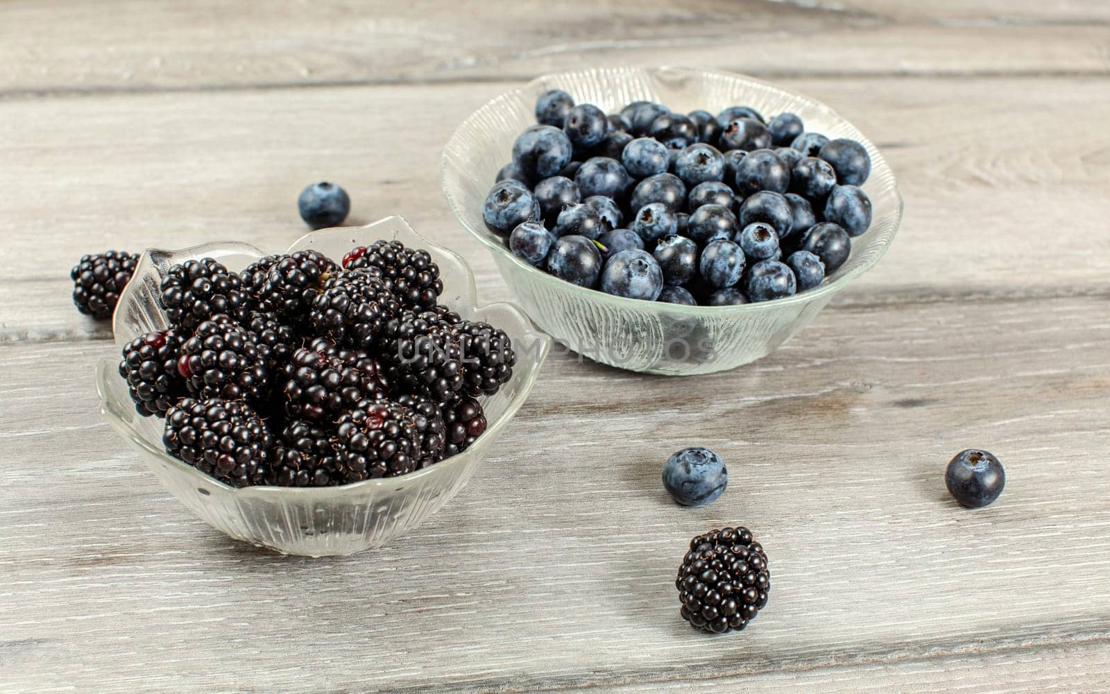 Small glass bowl of blueberries and blackberries on gray wood desk by Ivanko