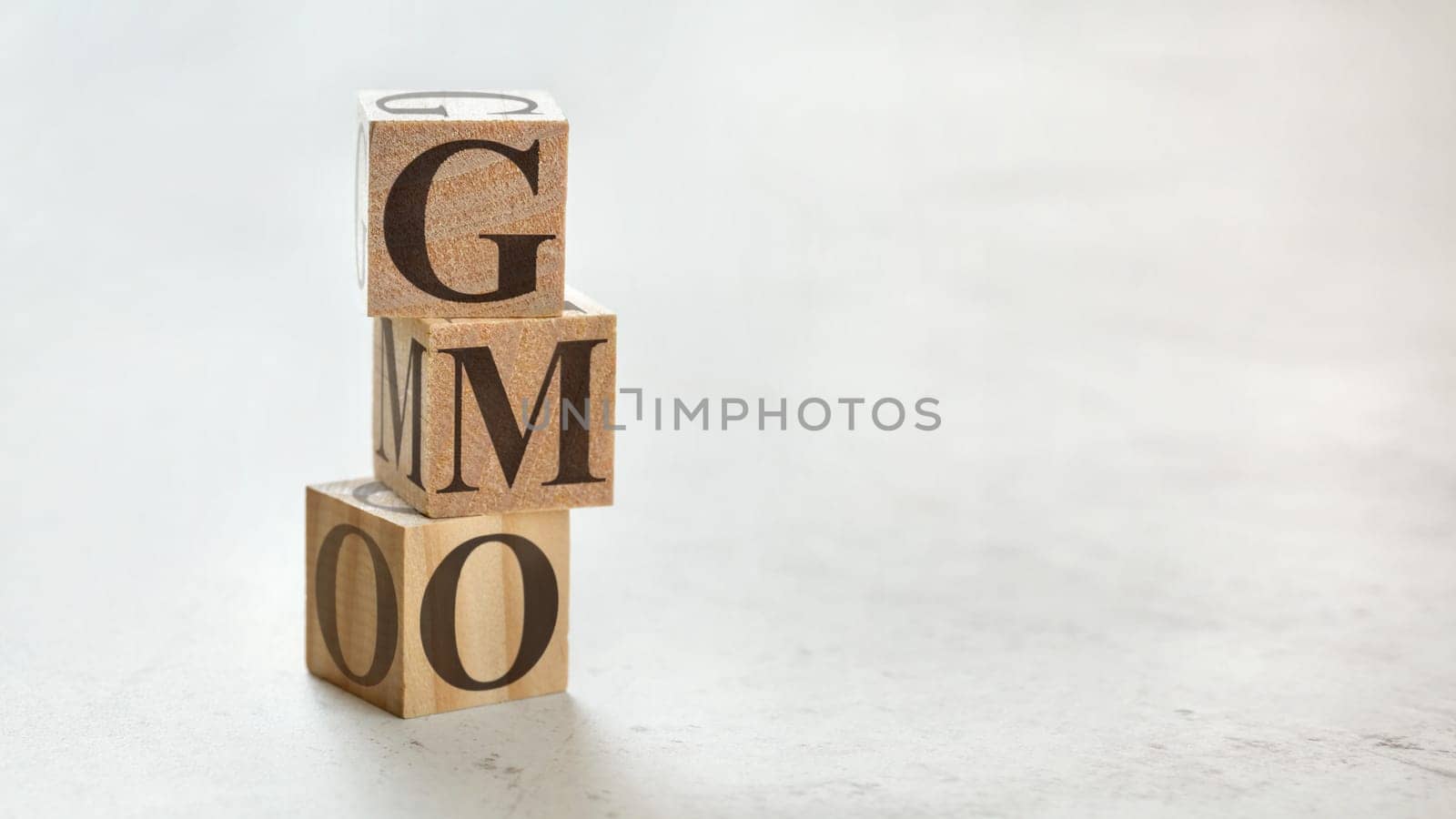 Pile with three wooden cubes - letters GMO meaning Genetically Modified Organism on them, space for more text / images at right side.