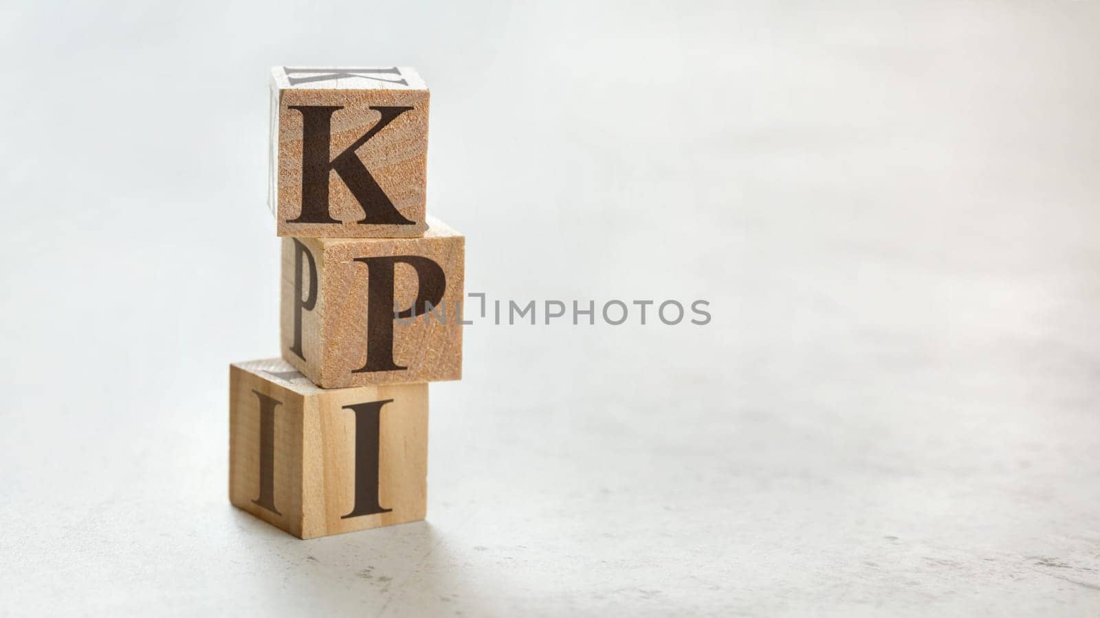 Pile with three wooden cubes - letters KPI meaning Key Performance Indicator on them, space for more text / images at right side.