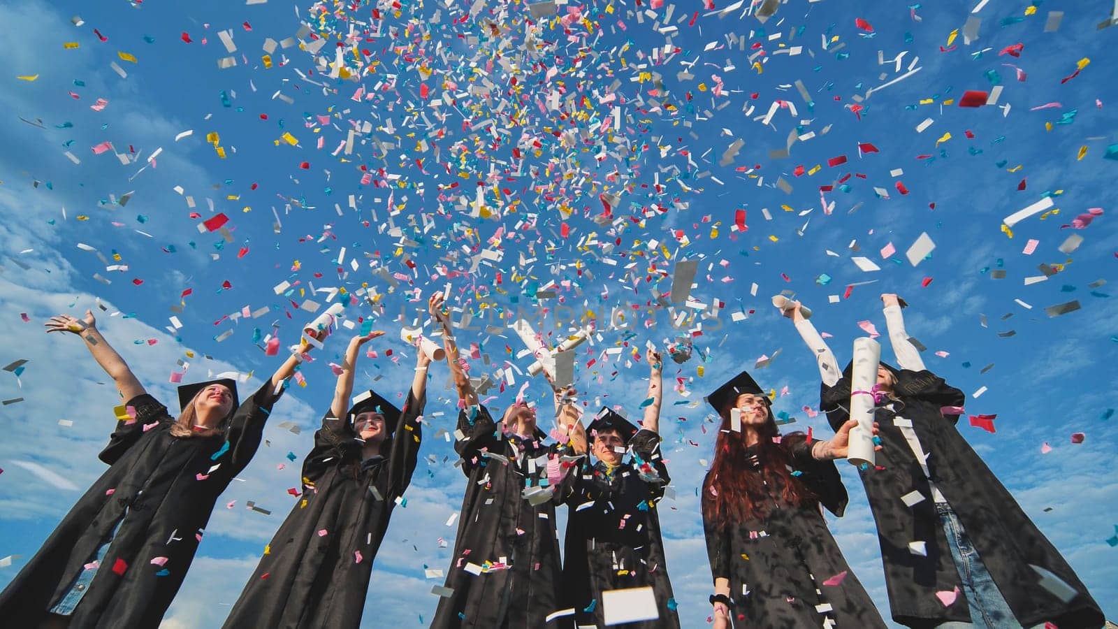 Graduates throw colorful confetti against a blue sky