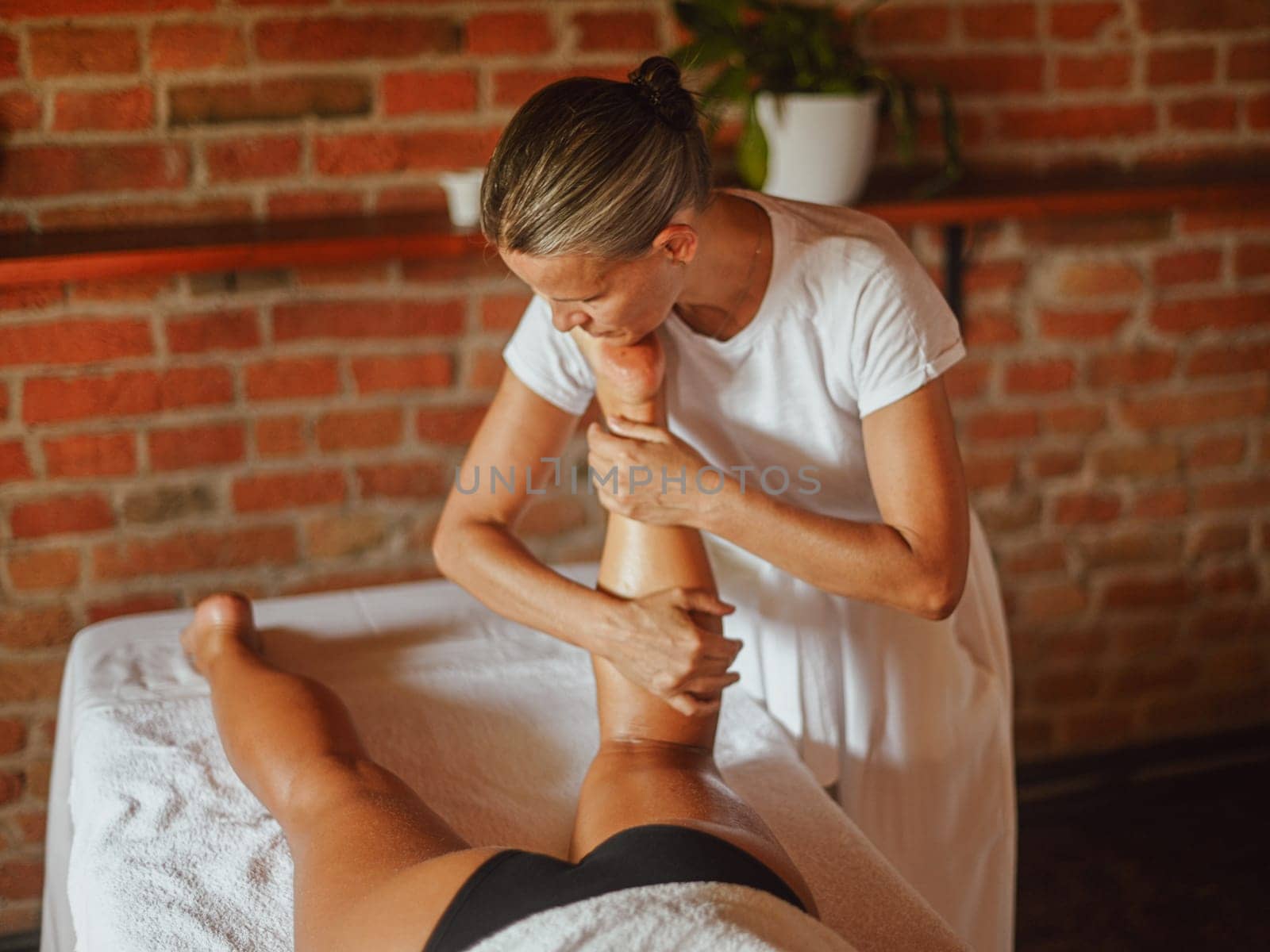 professional caucasian female physiotherapist masseuse performing leg massage to hispanic latino brunette woman in spa clinic