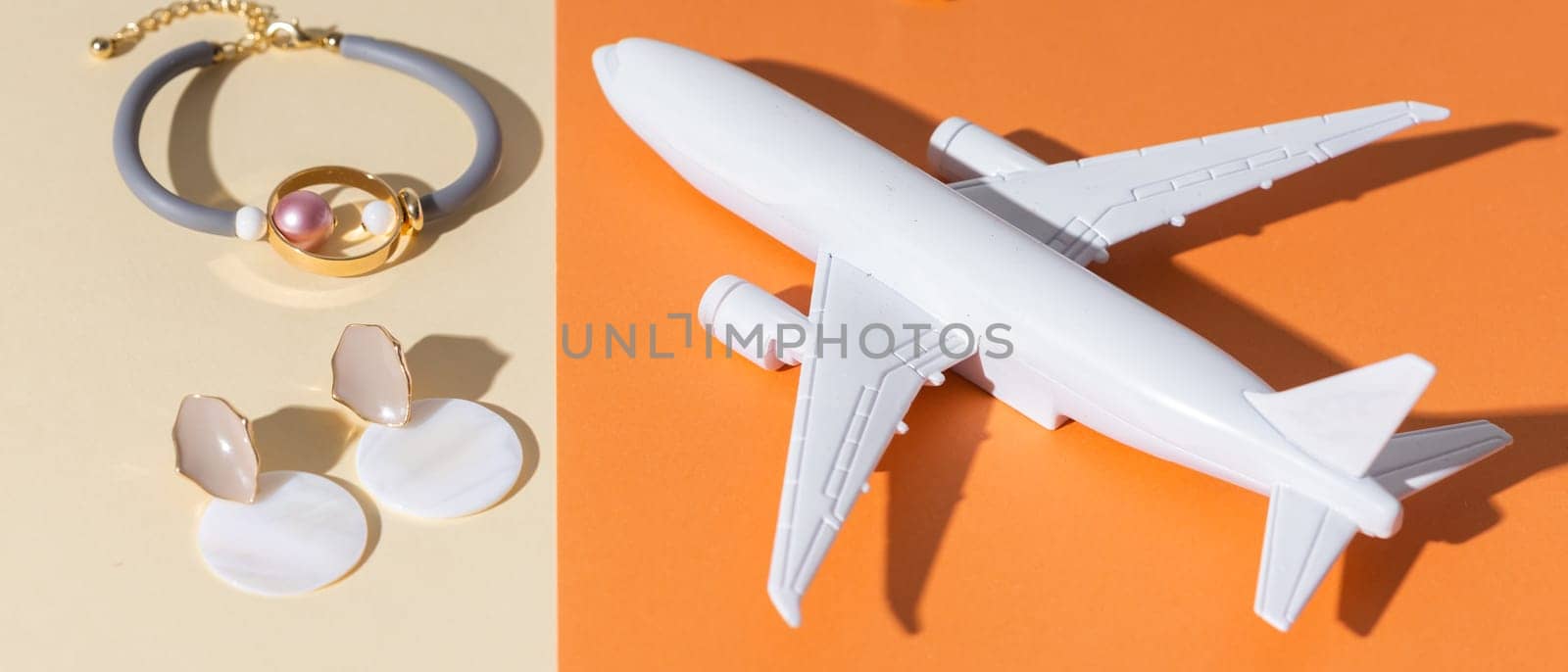 Modern minimalist handmade jewelry on orange and beige. Air plane toy for delivery and parcels on gift concept. Bracelets and earrings. Deliver handmade jewellery and accessories concept.