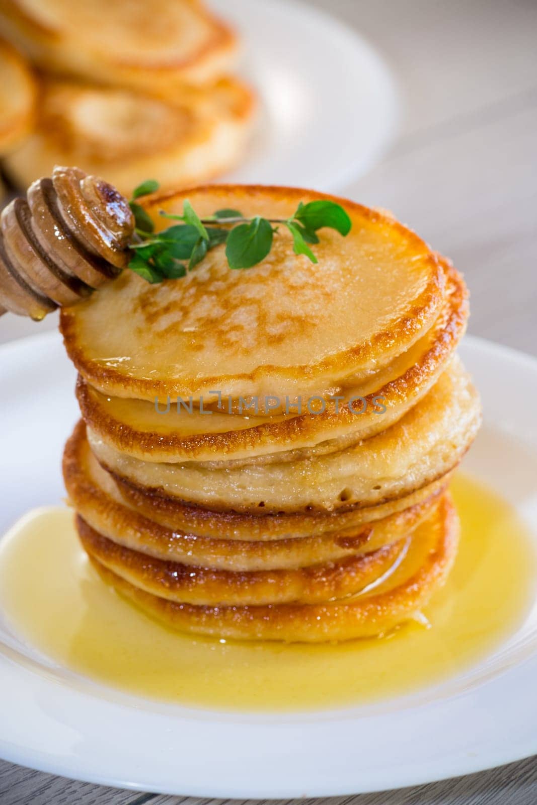 cooked sweet pancakes with honey in a plate on a light wooden table.