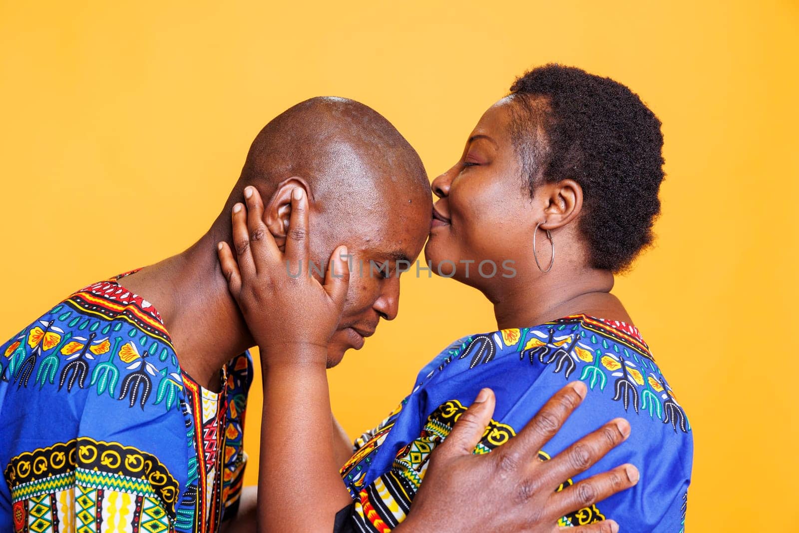 African american woman kissing husband in forehead, showing love and care. Black boyfriend and girlfriend showcasing affection and romance in relationship while posing in studio