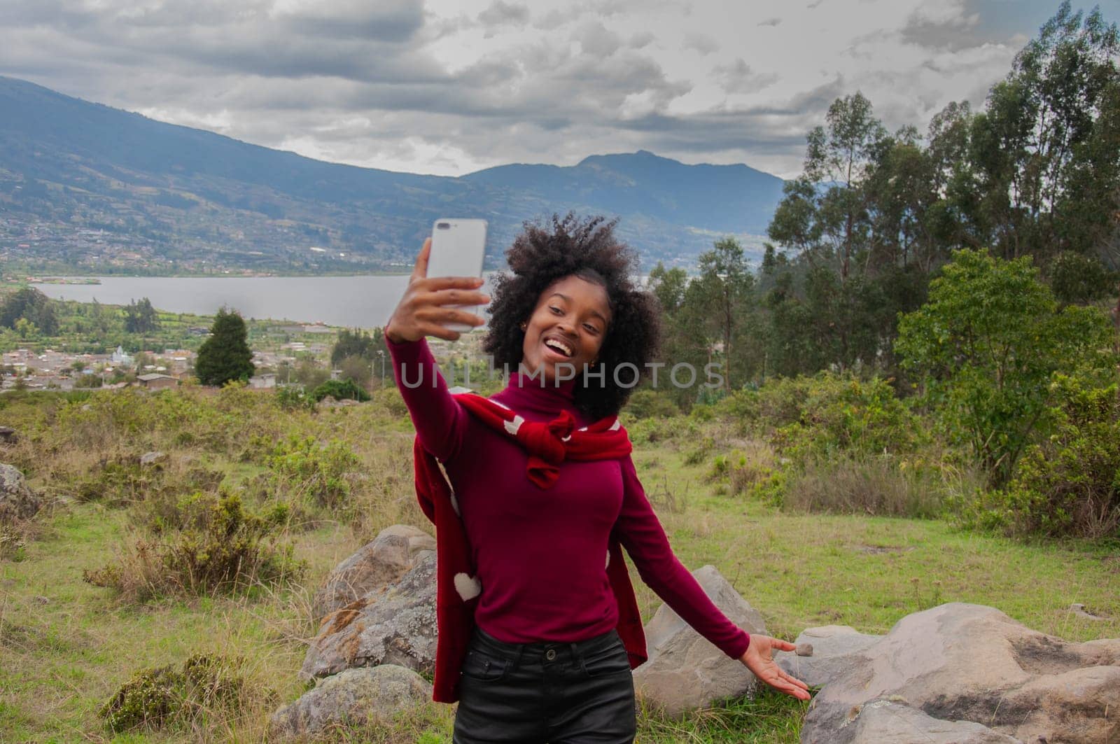 smiling and excited afro blogger girl showing her followers a lagoon in the mountains. High quality photo