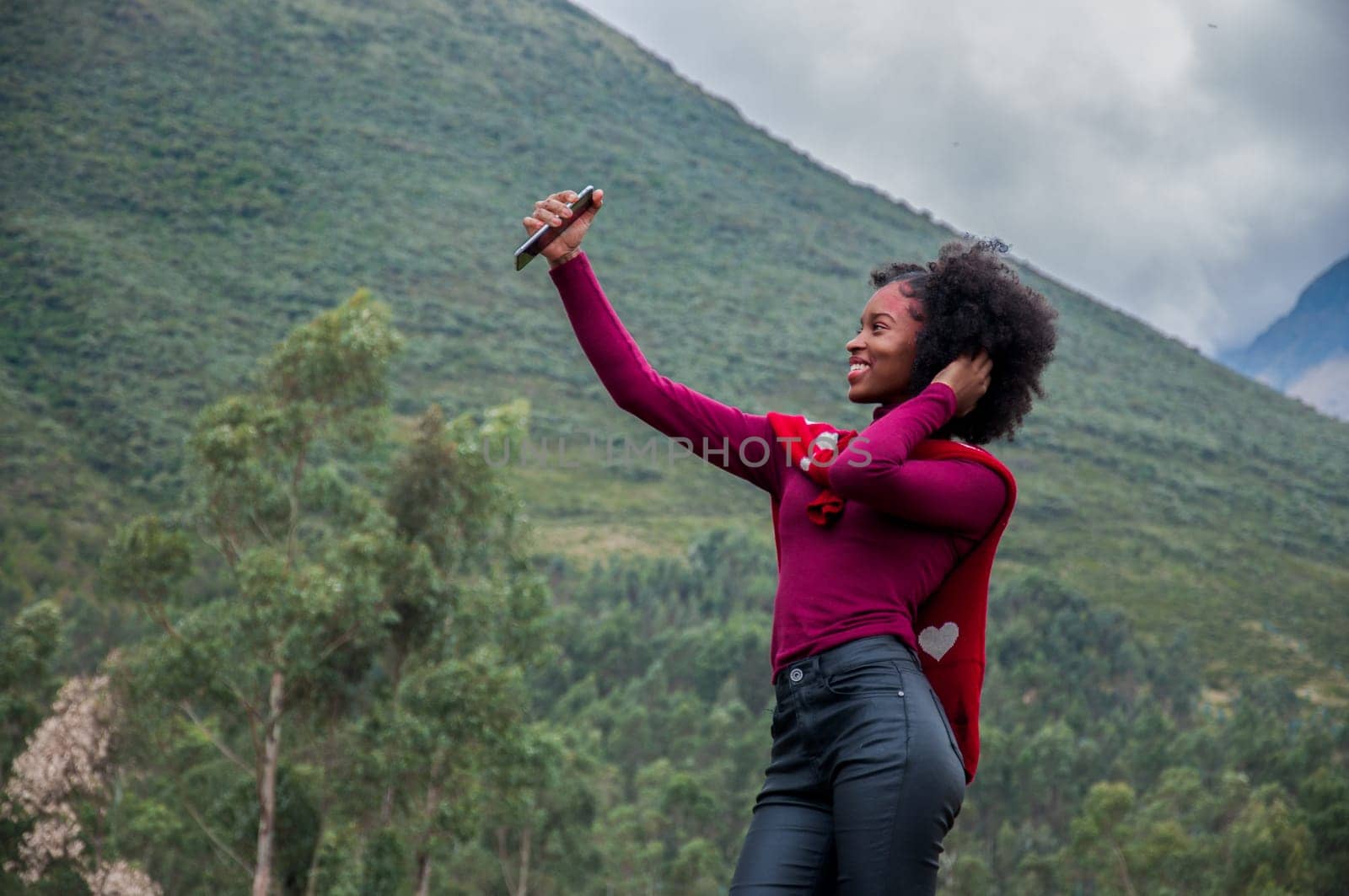 pretty smiling afro girl in black pants and red sweater doing a live broadcast next to a volcano. High quality photo