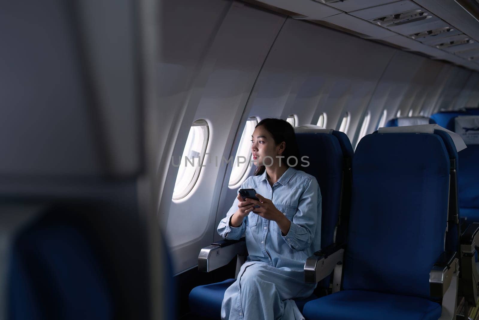 Asian people female person onboard, airplane window, using mobile while on the plane by itchaznong