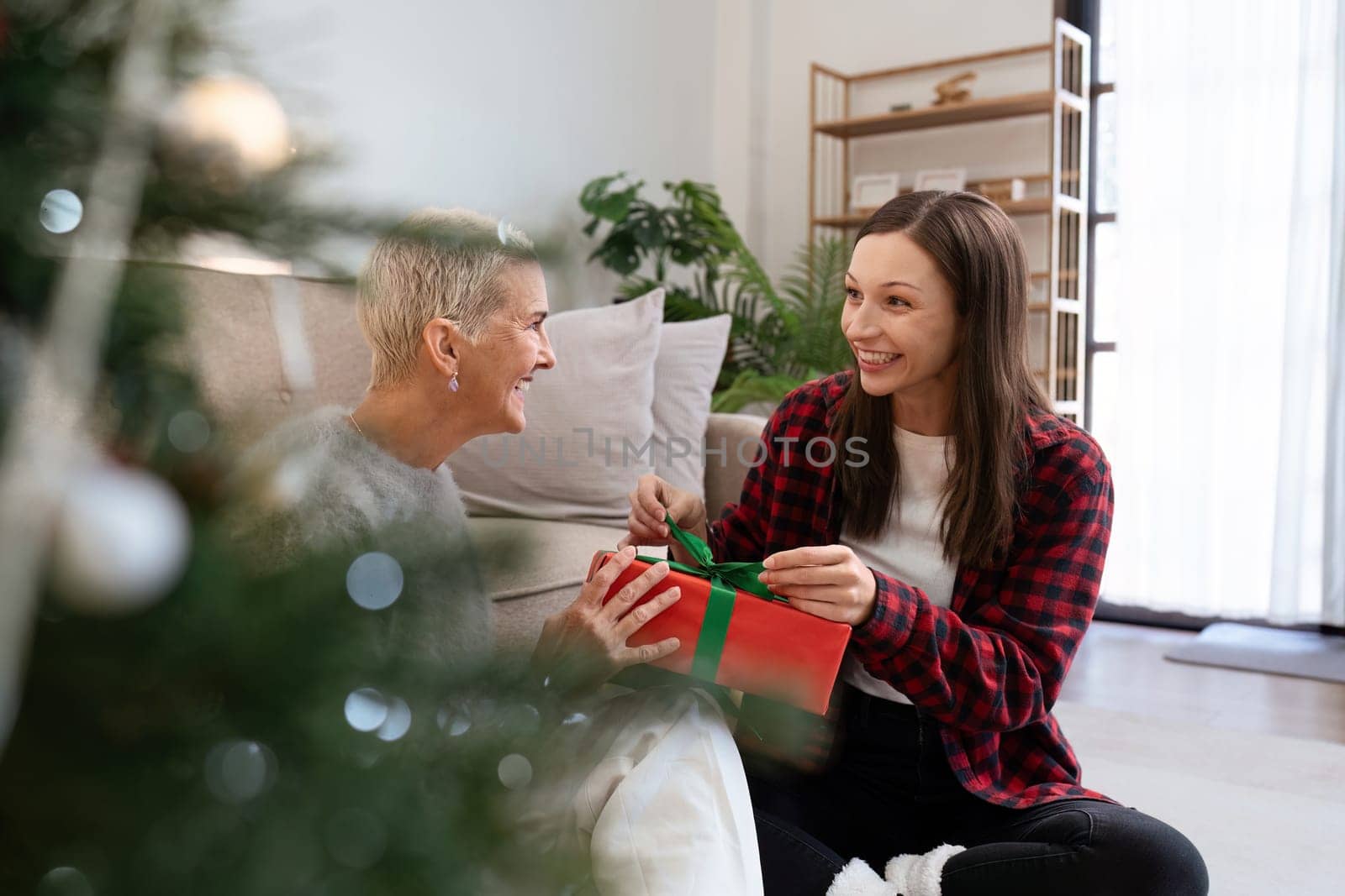 Daughter open gift from mother of Christmas while sitting on floor at home by itchaznong