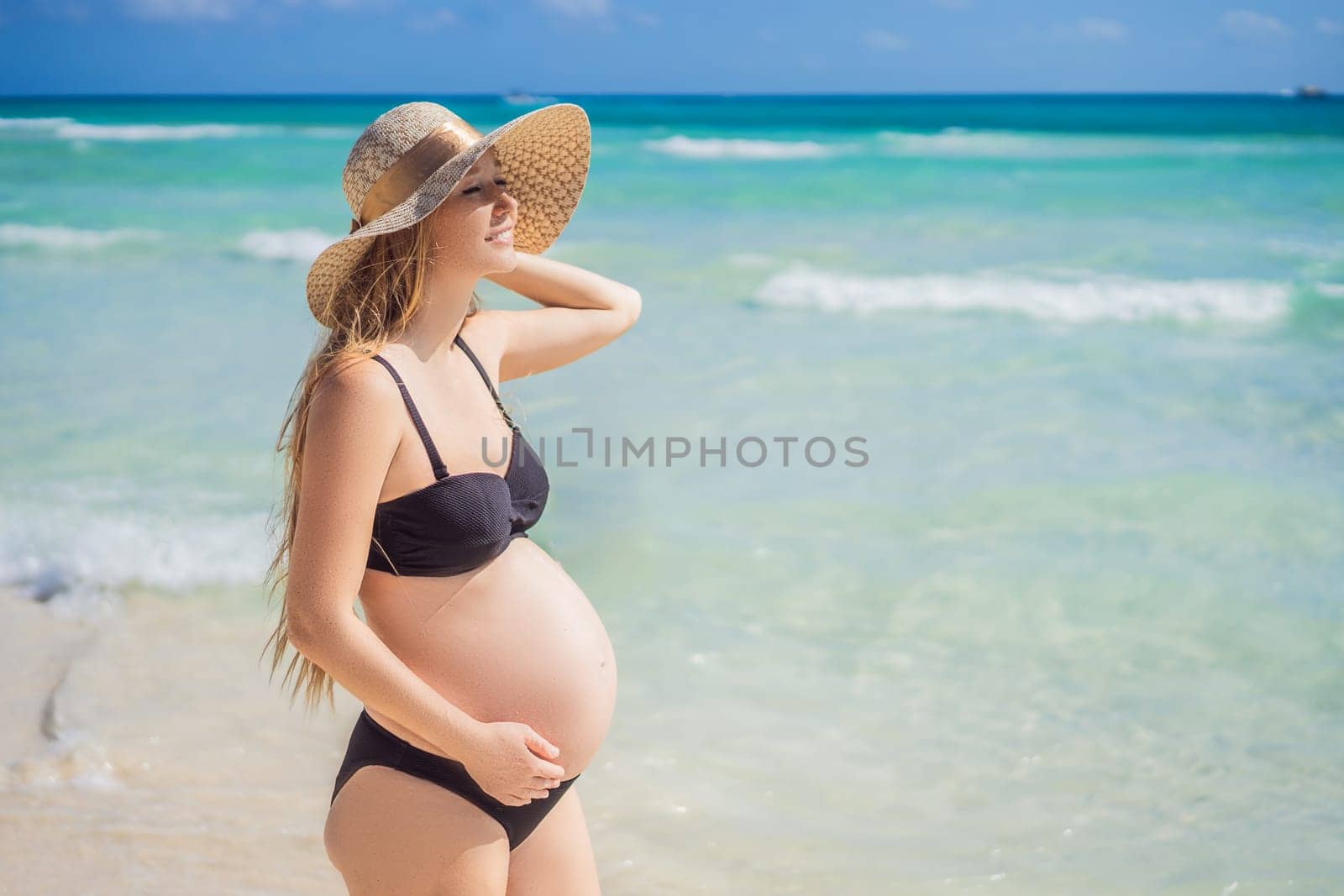 Radiant and expecting, a pregnant woman stands on a pristine snow-white tropical beach, celebrating the miracle of life against a backdrop of natural beauty.