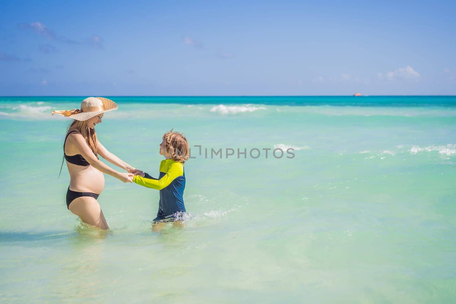 A radiant pregnant mother and her excited son share a tender moment on a serene, snow-white beach, celebrating family love amidst nature's beauty by galitskaya