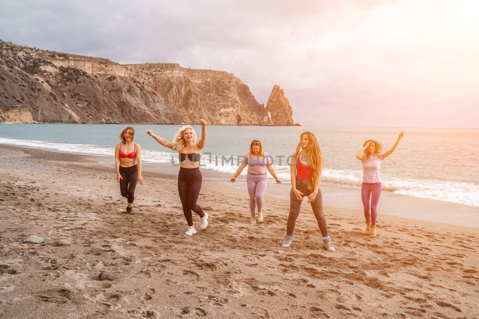 A group of five female friends are doing exercises on the beach. Beach holiday concept, healthy lifestyle.