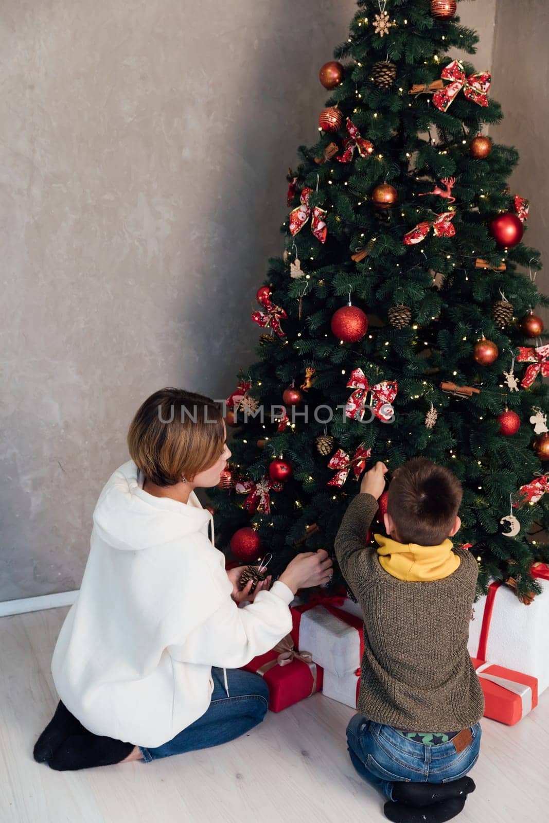 Mom with boy decorating christmas tree with gifts for new year by Simakov