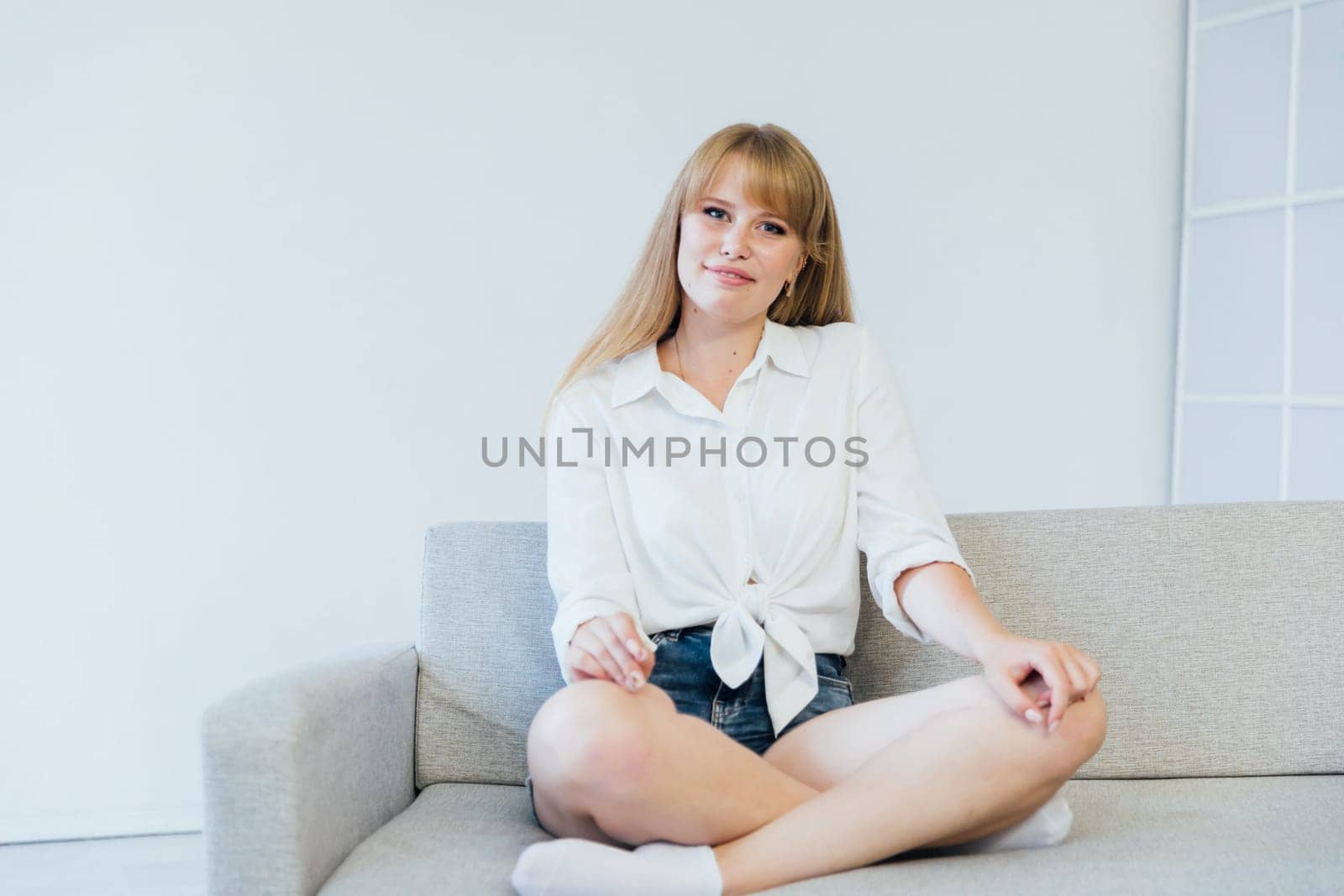 Beautiful young woman smiling sitting on sofa at home by Simakov
