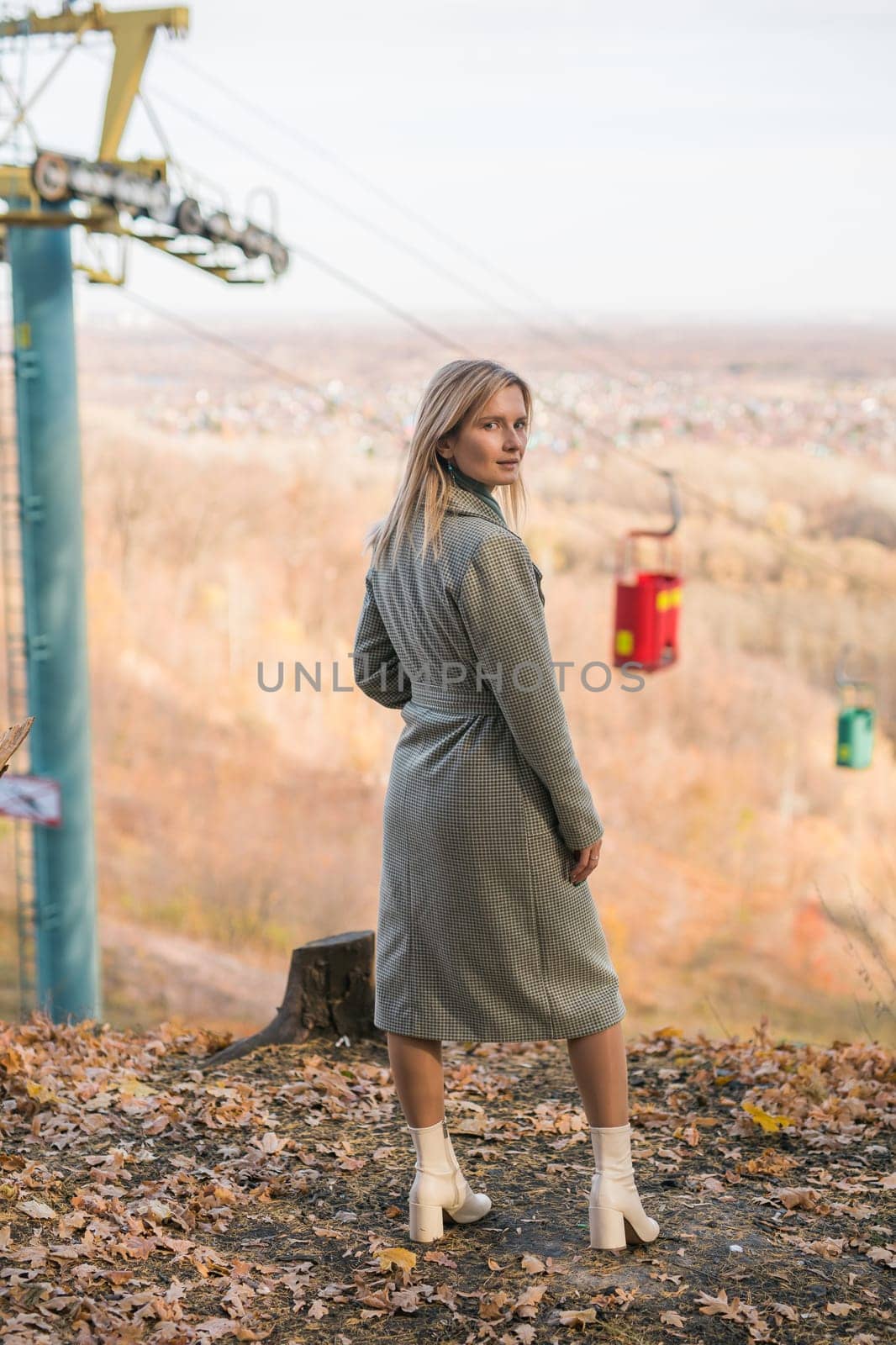 Blonde woman in elegant gray coat walks in the sunny autumn season park. Generation z and gen z youth concept