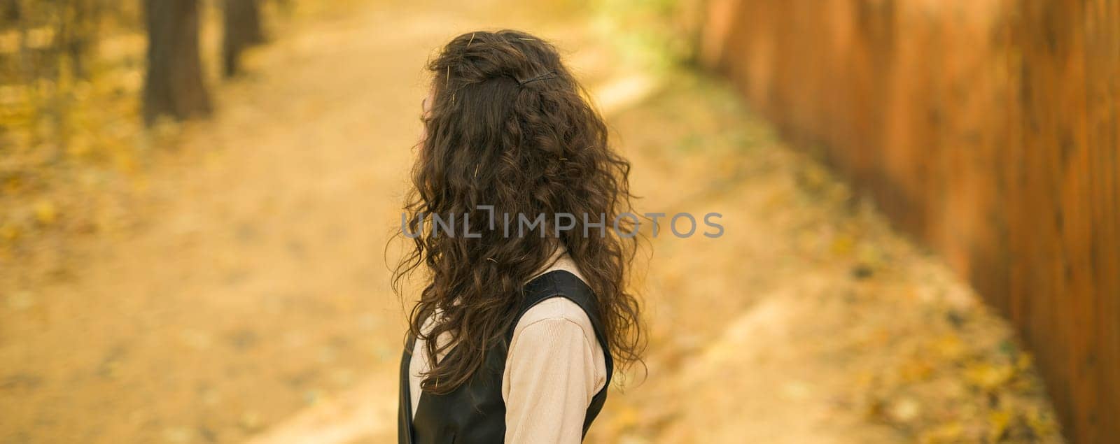 Banner Girl in fall park back view copy space. Woman with long curly hair. Beautiful sunlight in forest. Hair care. Millennial Generation and youth. by Satura86