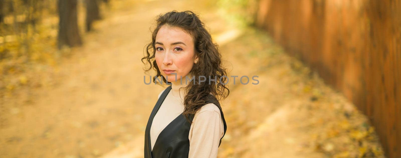 Attractive young woman walking in autumn park, happy mood and fashion style trend and curly long brown hair. Fall season and pretty female portrait. Millennial generation