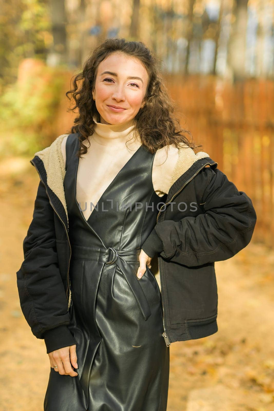 Attractive young woman walking in autumn park, happy mood and fashion style trend and curly long brown hair. Fall season and pretty female portrait. Millennial generation