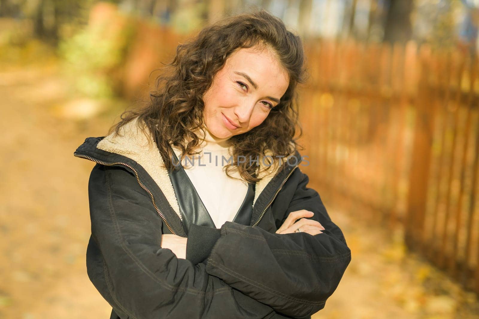 Attractive young woman walking in autumn park, happy mood and fashion style trend and curly long brown hair. Fall season and pretty female portrait. Millennial generation