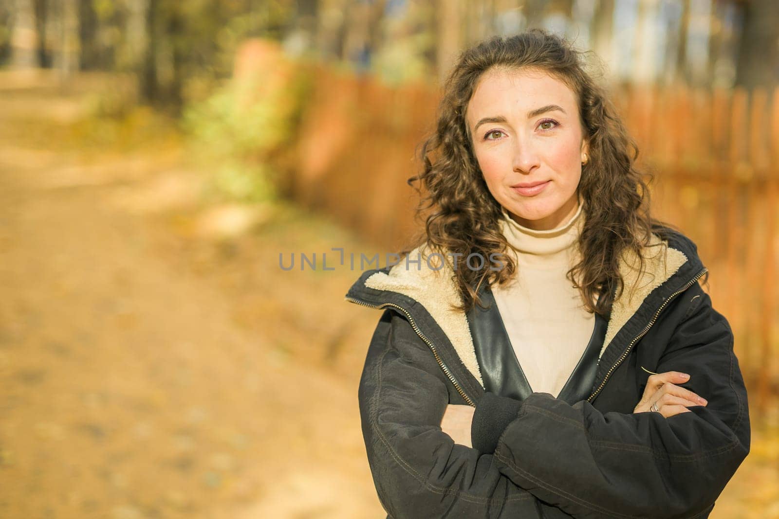 Attractive young woman walking in autumn park, happy mood and fashion style trend and curly long brown hair. Fall season and pretty female portrait. Millennial generation