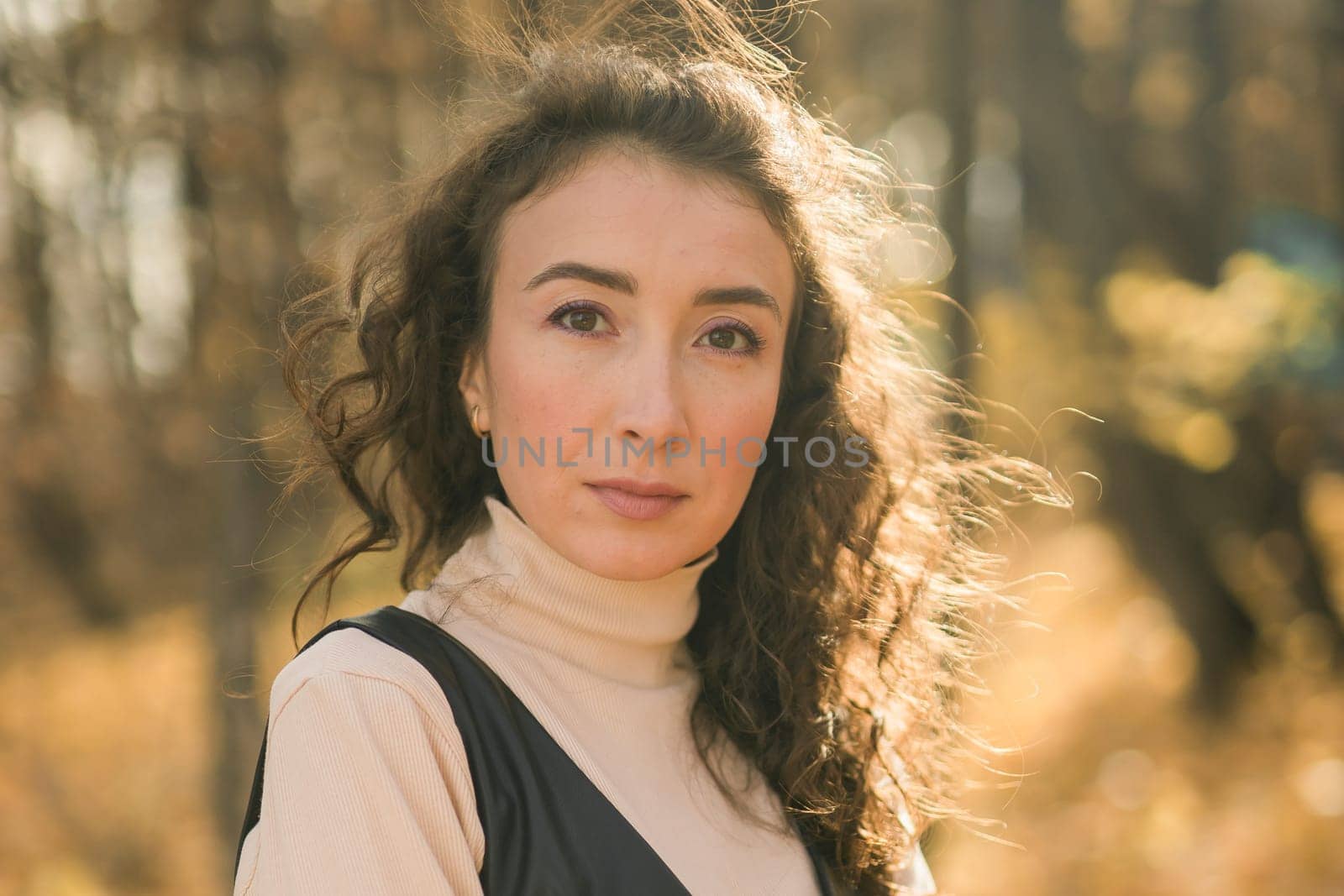 Attractive young woman walking in autumn park, happy mood and fashion style trend and curly long brown hair. Fall season and pretty female portrait. Millennial generation