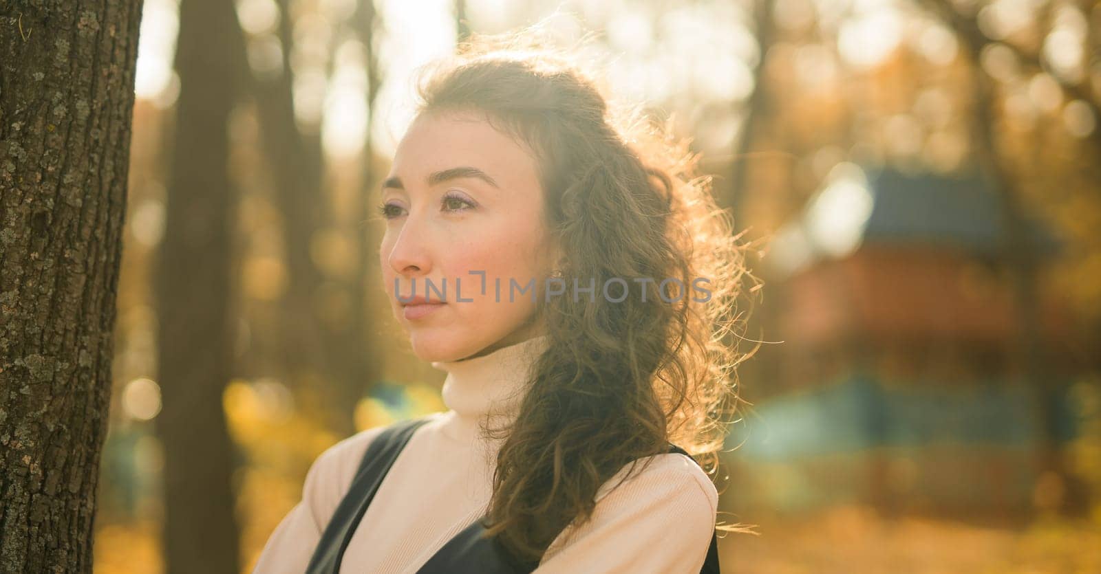 Attractive young woman walking in autumn park, happy mood and fashion style trend and curly long brown hair. Fall season and pretty female portrait. Millennial generation