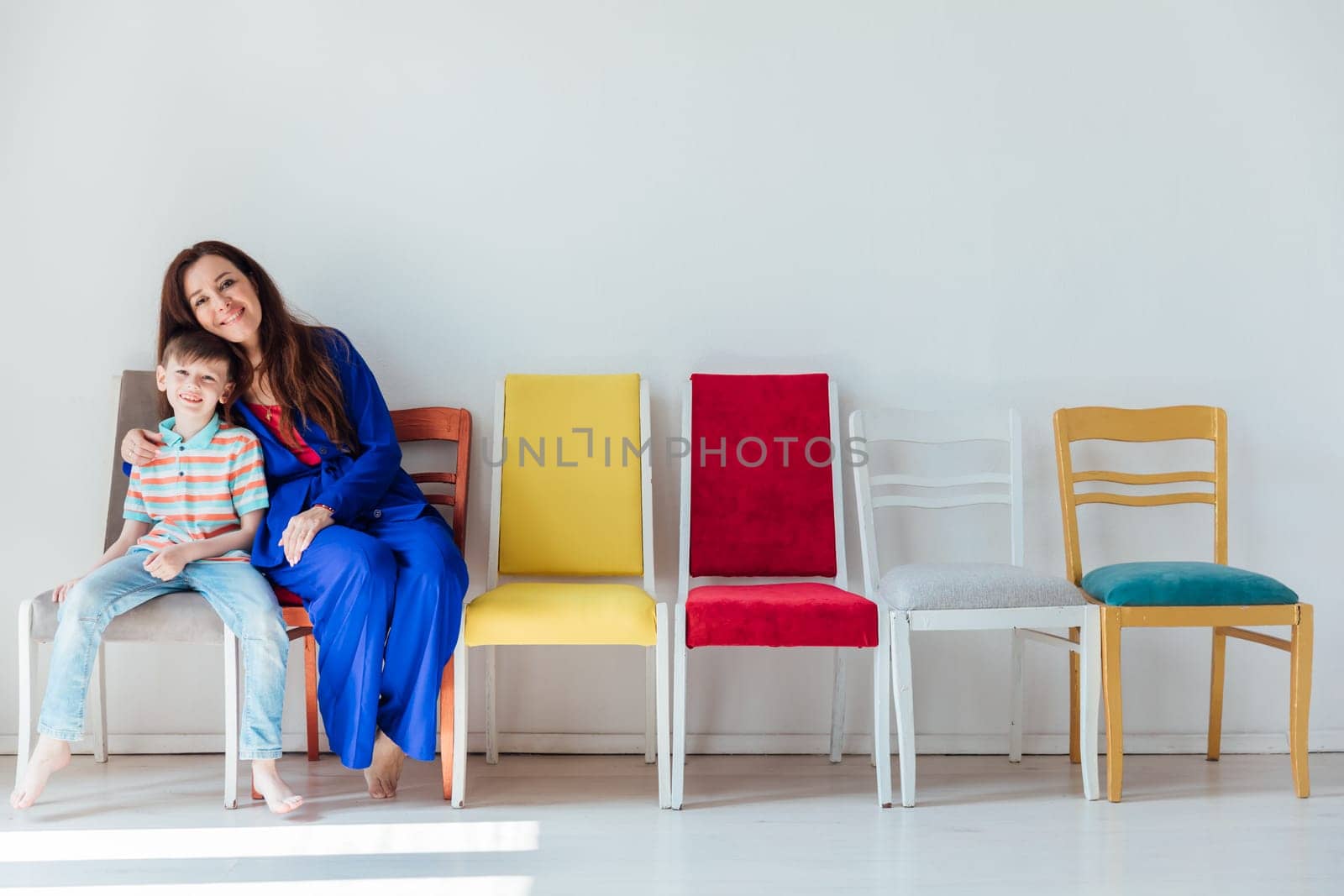 Mom with little boy sitting on colored chairs having fun by Simakov