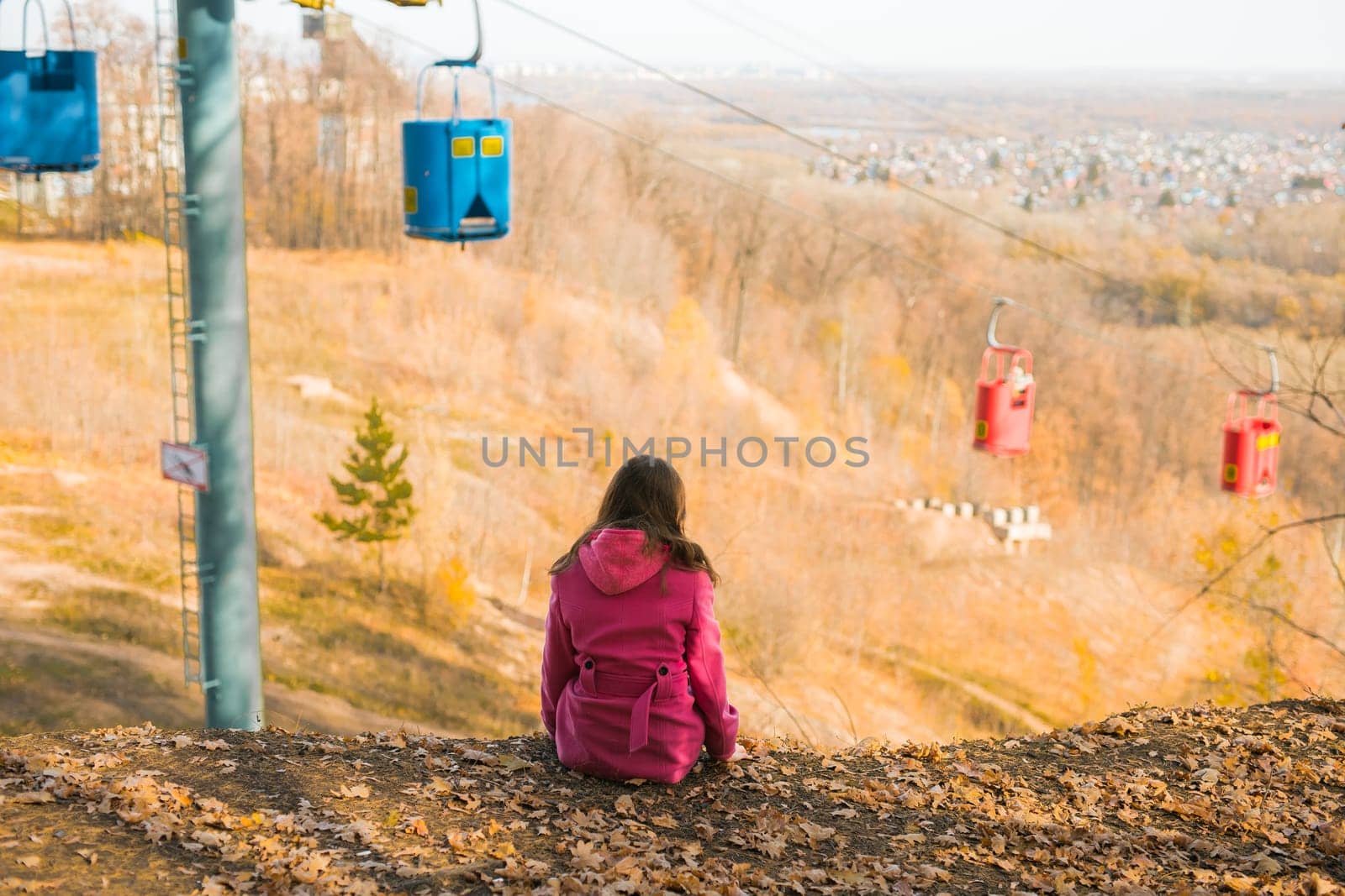 Back view of a girl woman resting on autumn park in fall season and look at the cable car. Generation Z and gen z youth. Copy empty space for text