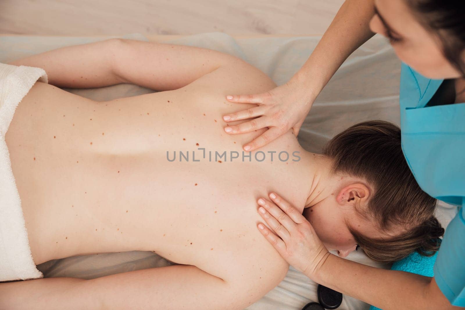 Masseuse doing a therapeutic relaxing back massage to a girl in the spa by Simakov