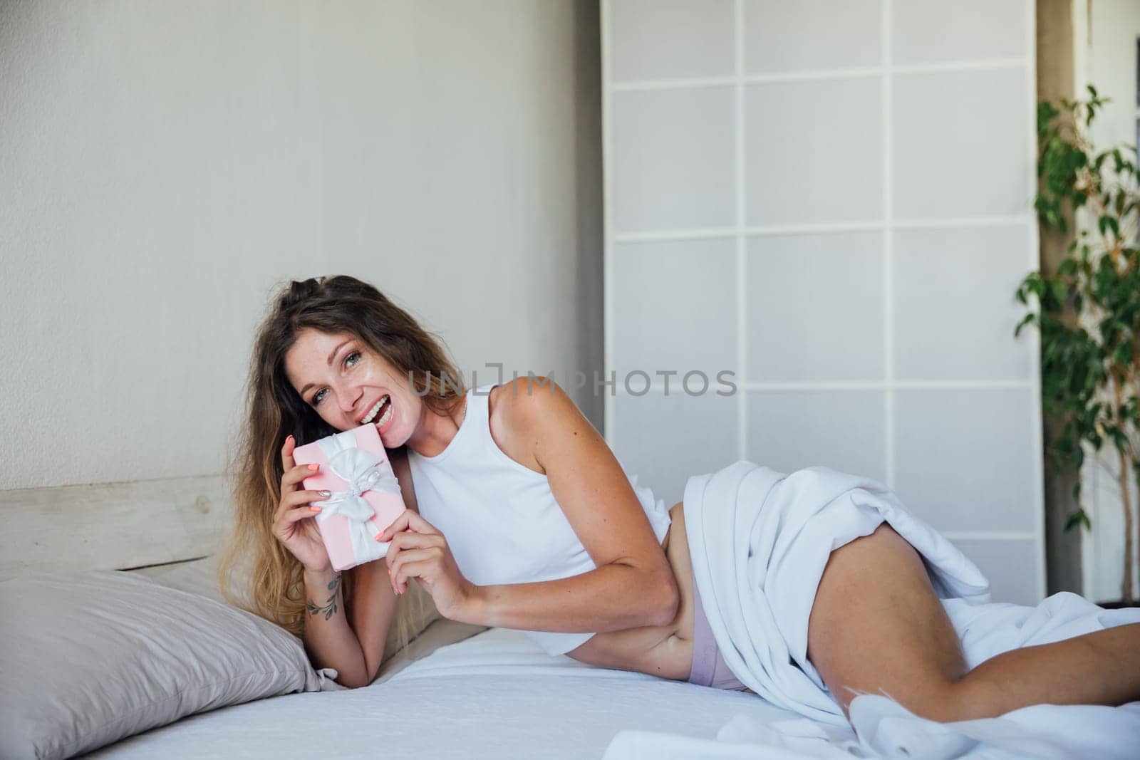 Smiling woman with gift box lying in bed and looking at camera