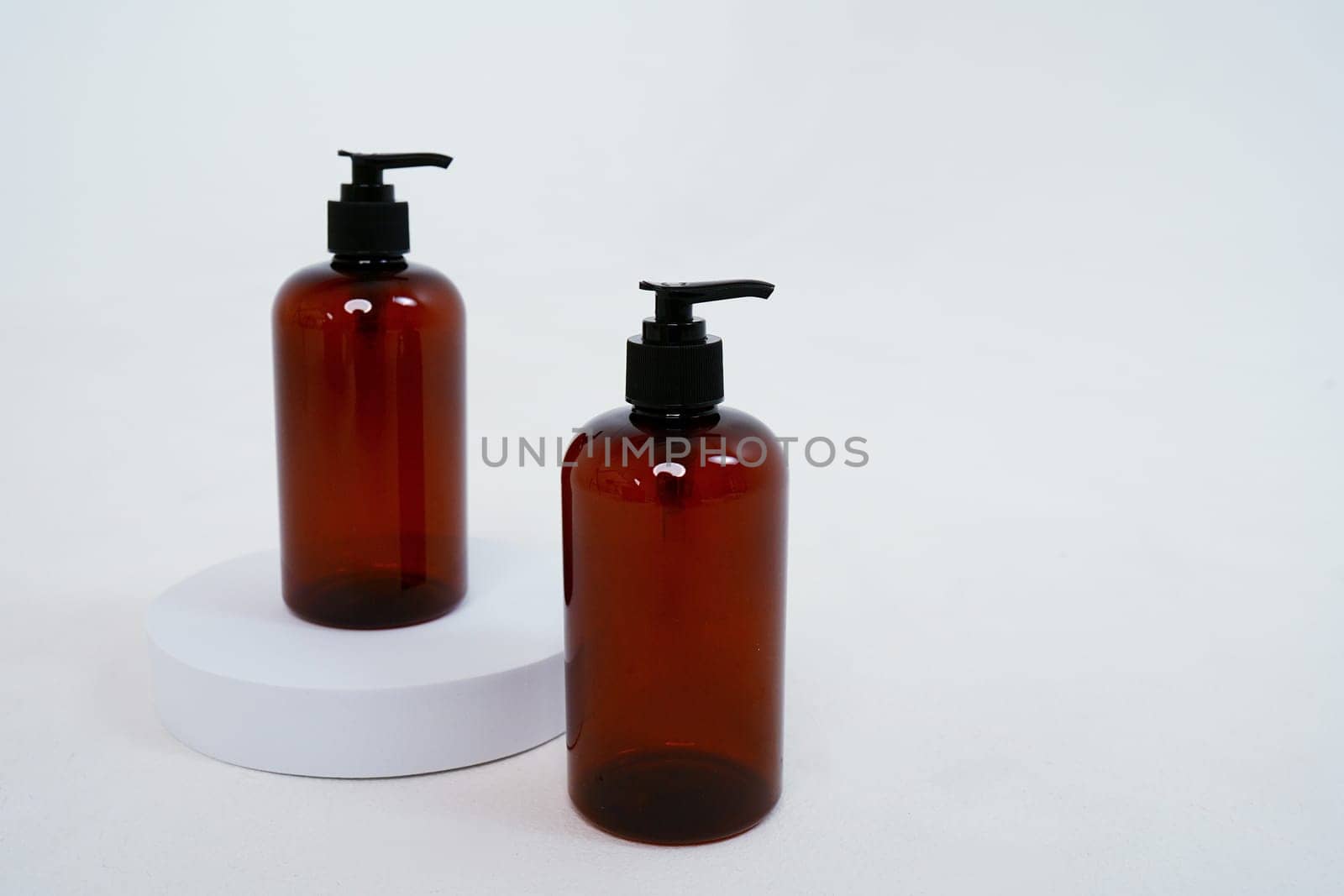 Two dark bottles with soap dispenser on a light background, on a stand. isolated on white background by tewolf