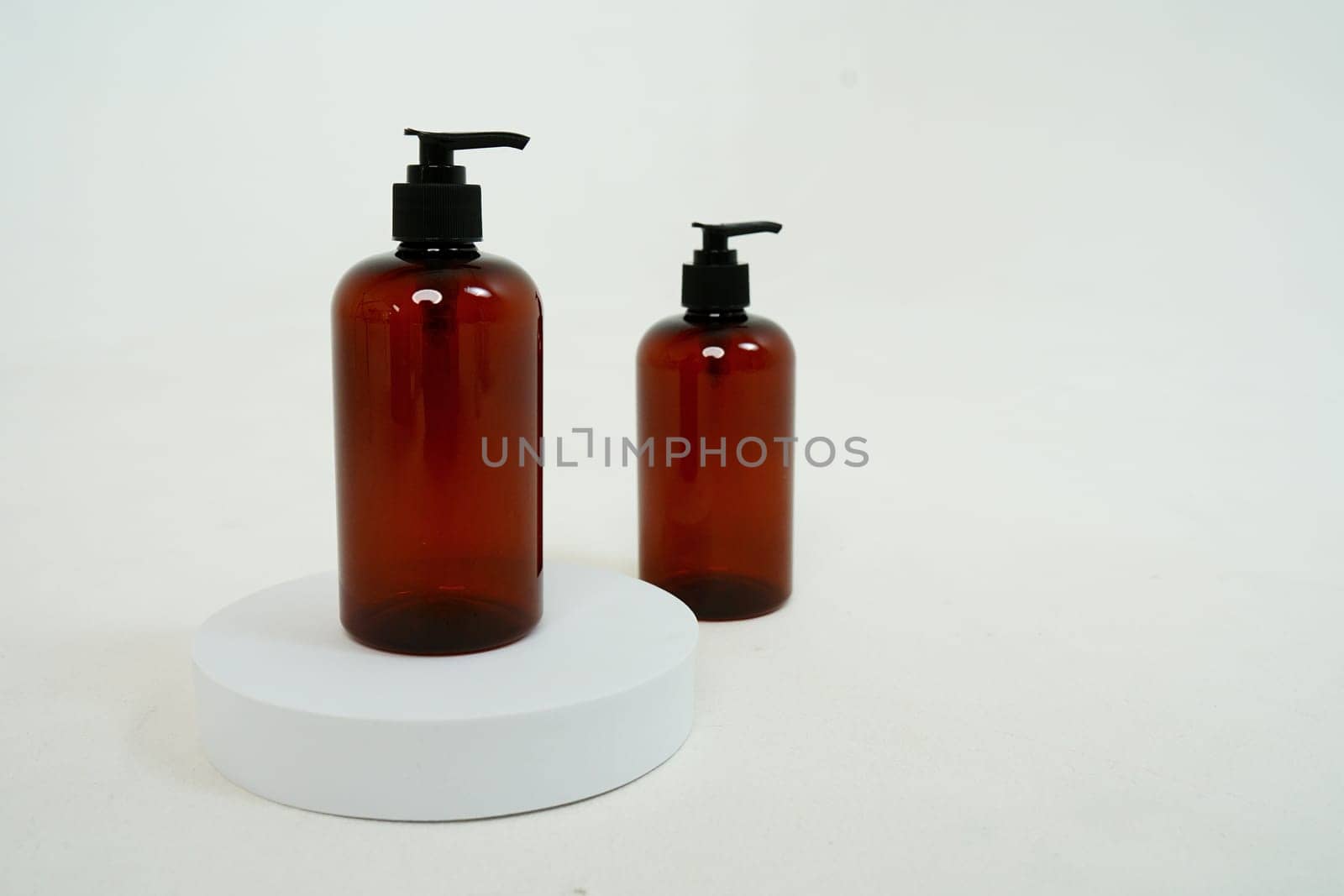Two dark bottles with soap dispenser on a light background, on a stand. isolated on white background by tewolf