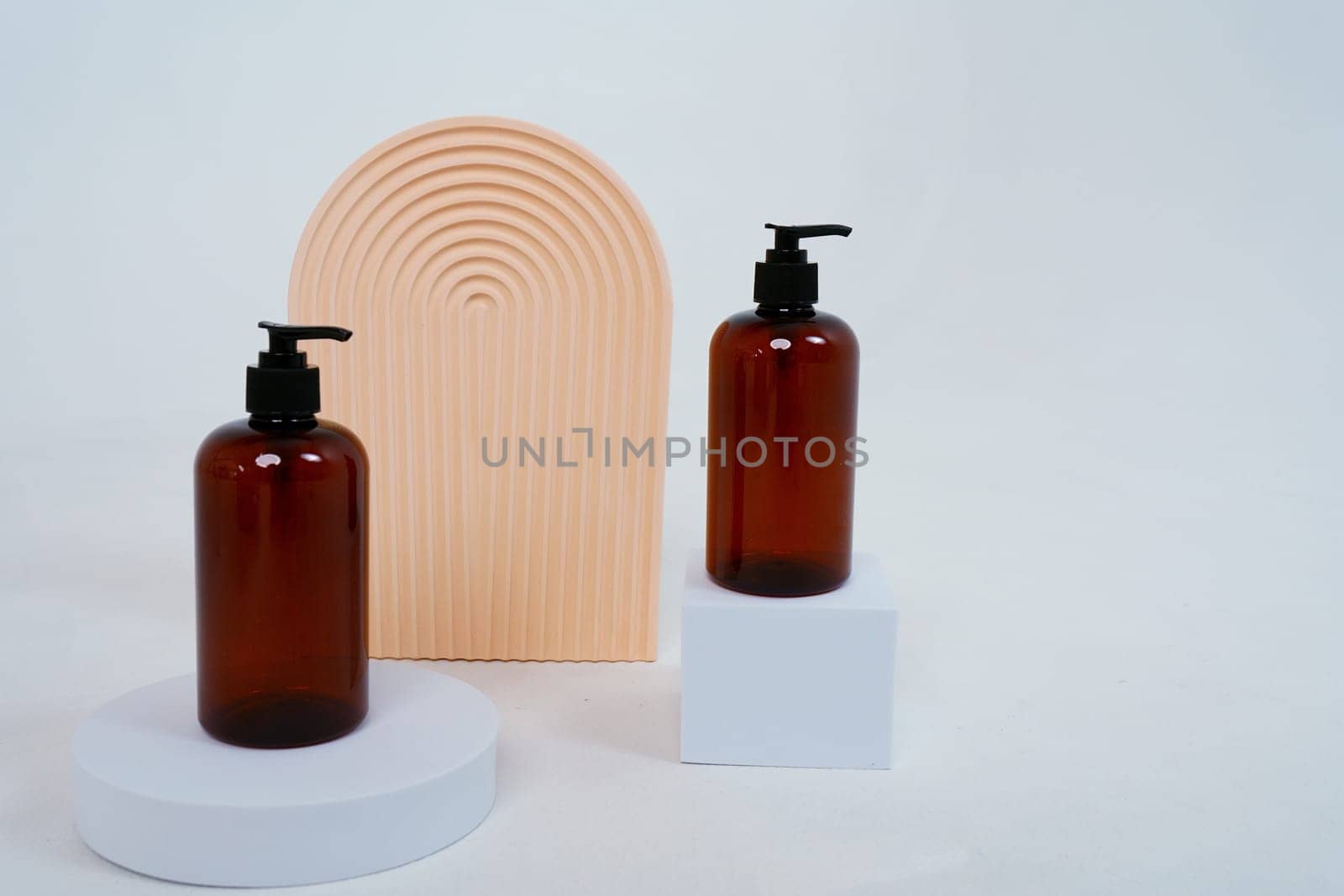 Composition with geometric shapes and natural body care cosmetics Dark zero waste glass bottles with dispenser standing on a light gray background. Advertising concept. High quality photo