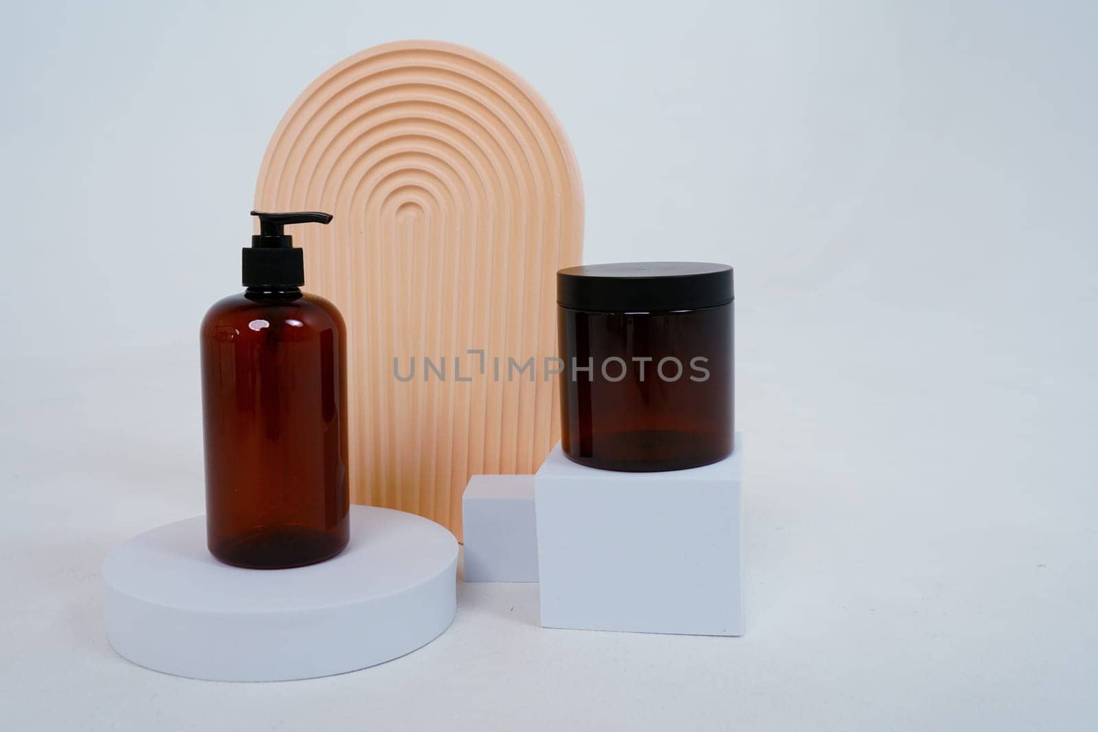 Composition with geometric shapes and natural cosmetics for body care. Glass bottle with a dispenser and a jar of cream, on a light gray background. Advertising concept. High quality photo