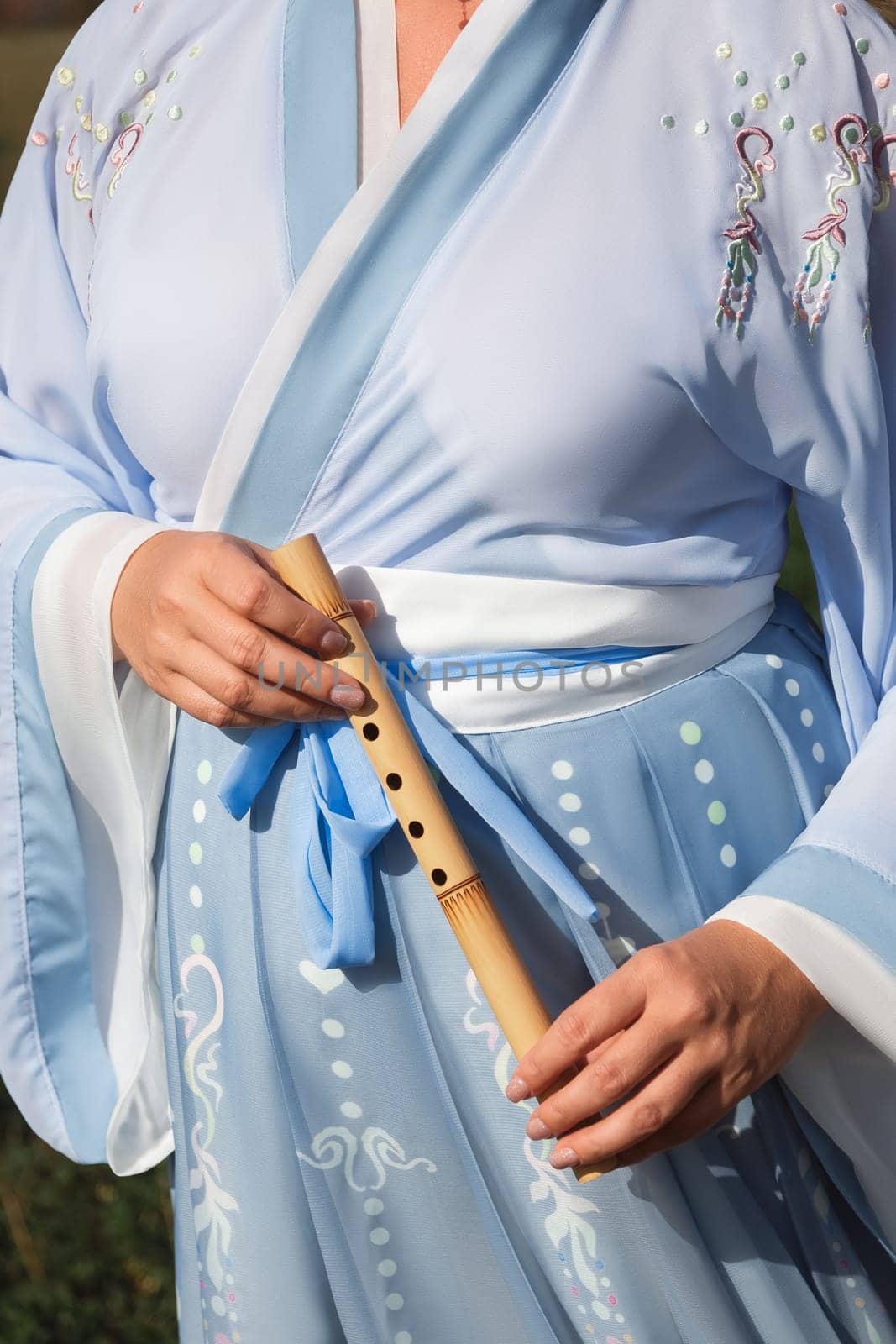 A woman in a traditional Chinese hanfu dress holds a bamboo flute close-up