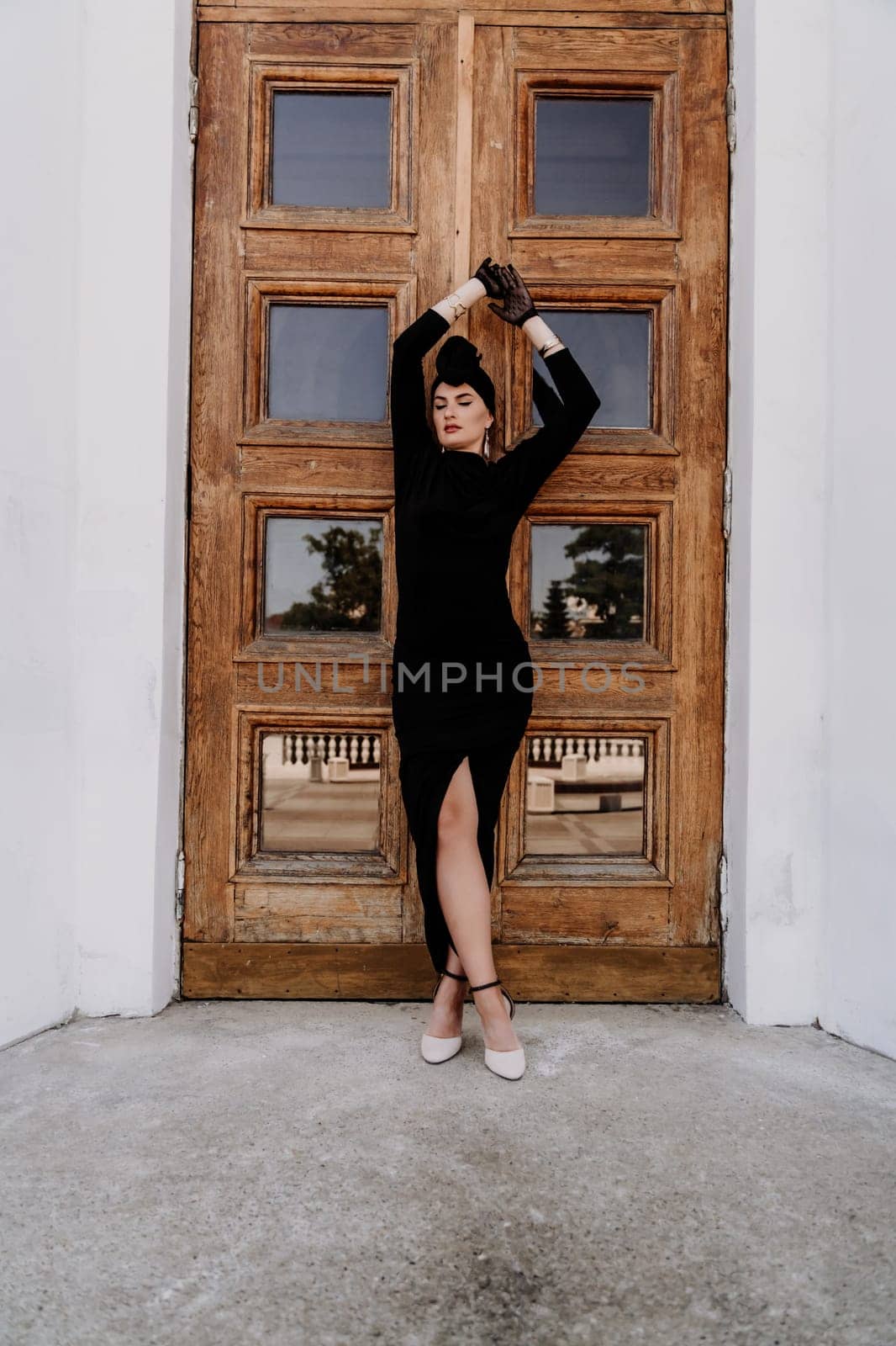 Stylish woman in the city. Fashion photo of a beautiful model in an elegant black dress posing against the backdrop of a building on a city street.