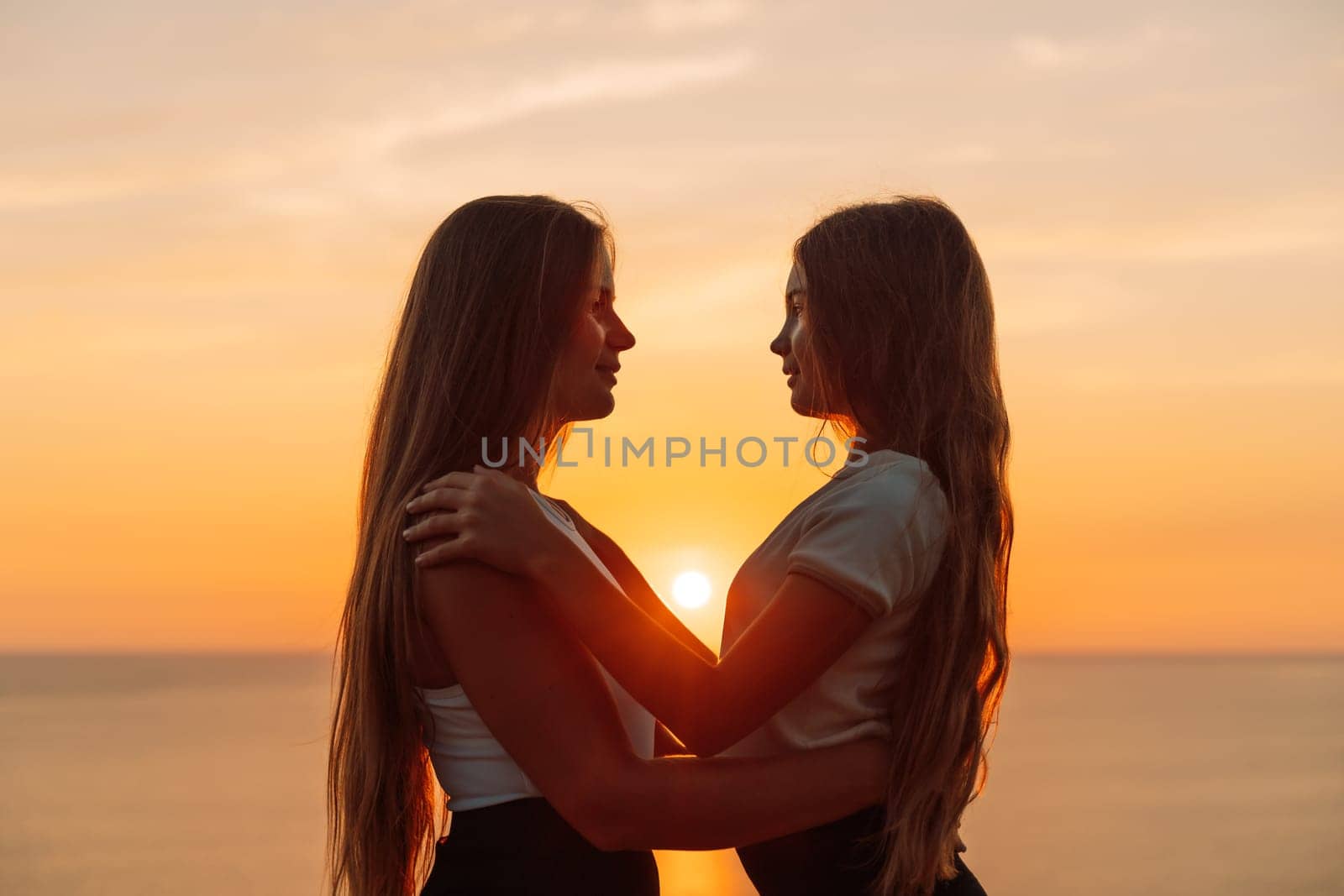 Mother daughter sunset. Mother and daughter stand on the beach, hugging and looking at each other enjoying the sunset. by Matiunina
