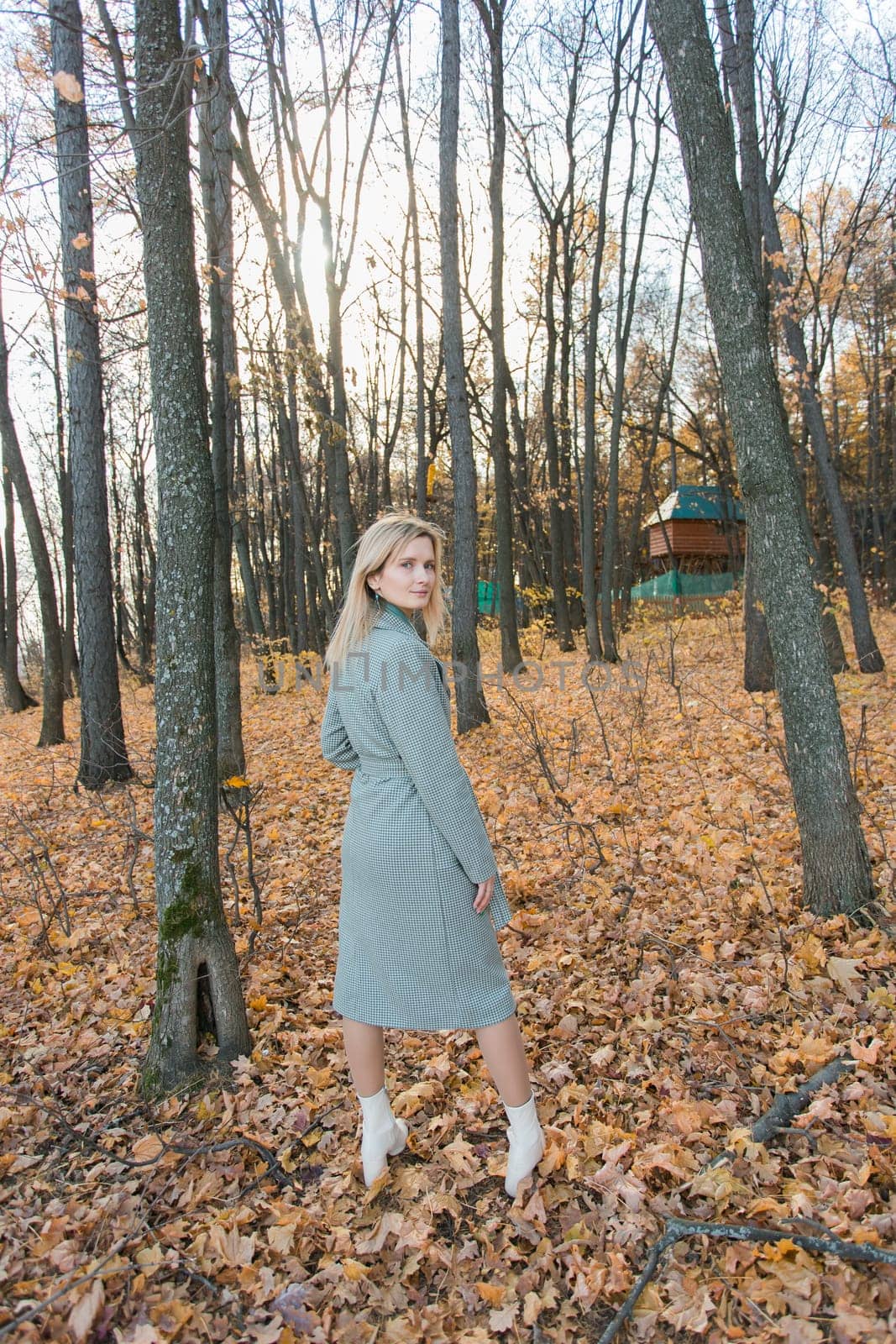 Blonde woman in elegant gray coat walks in the sunny autumn season park. Generation z and gen z youth concept