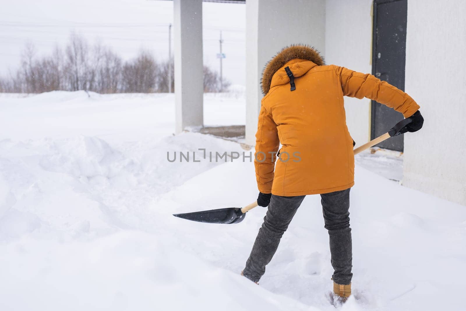 Young man clearing snow in his backyard village house with shovel. Remove snow from the sidewalk