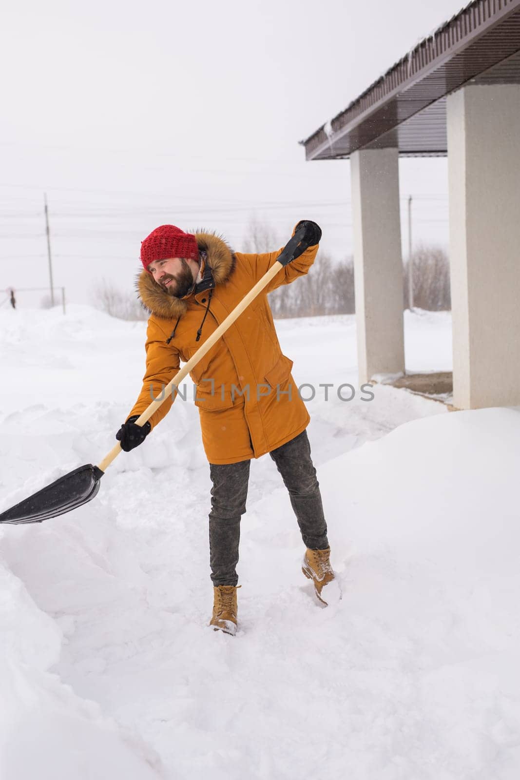 Young man clearing snow in his backyard village house with shovel. Remove snow from the sidewalk