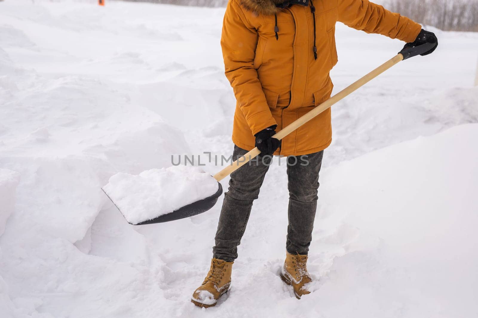 Close-up Young man clearing snow in his backyard village house with shovel. Remove snow from the sidewalk. by Satura86