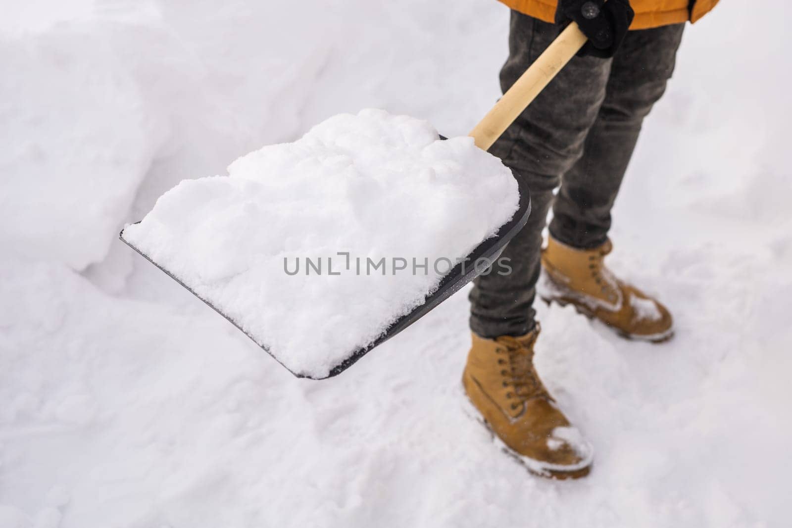 Close-up man cleaning snow from sidewalk and using snow shovel. Winter season by Satura86