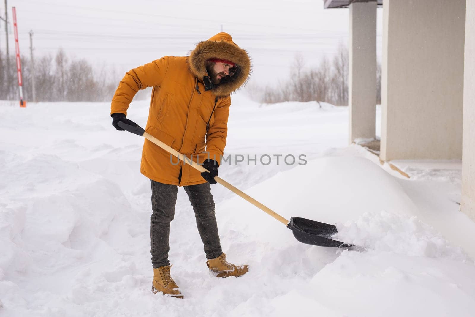 A man cleans and clears the snow in front of the house on frosty day. Cleaning the street from snow on a winter day. Snowfall and severe snowstorm in winter. by Satura86