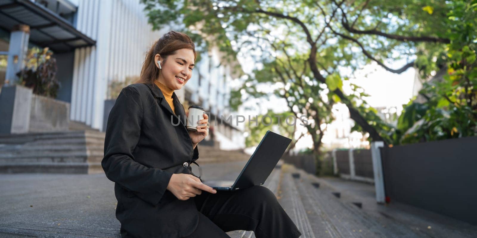 Smiling young Asian business woman using laptop sitting outdoor. hybrid working, searching job online thinking of digital solution by nateemee
