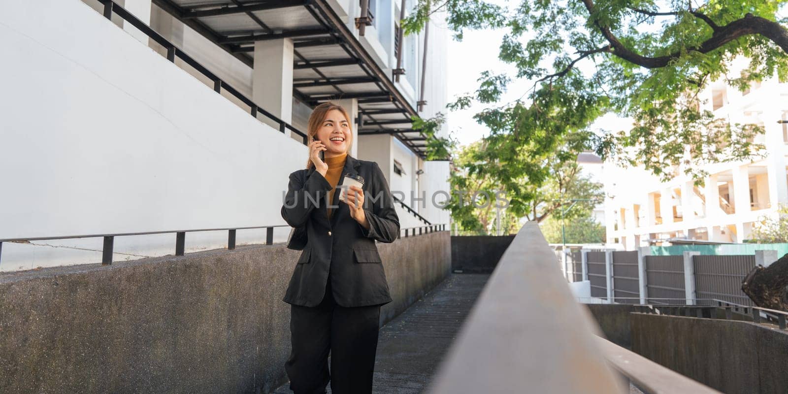 Successful business woman talking on mobile outdoor with holding hot coffee. beautiful woman going to working with coffee walking near office building by nateemee