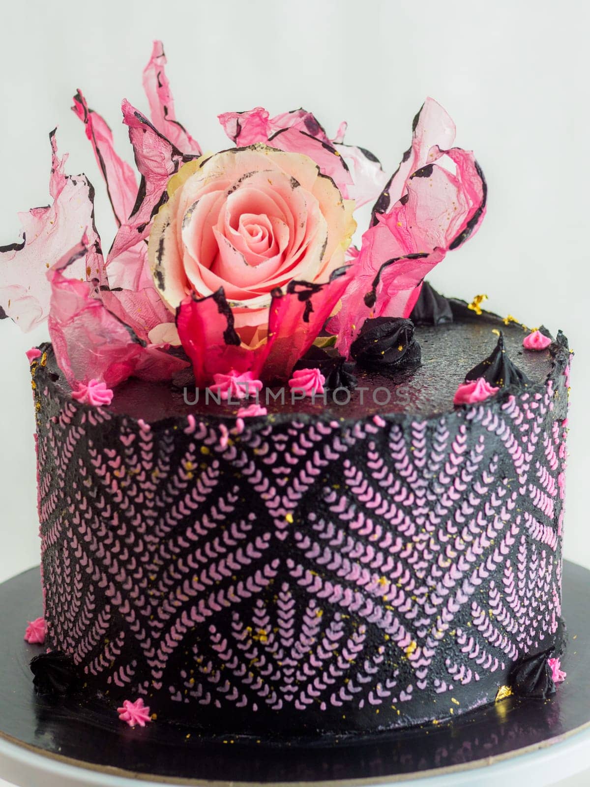 frosted icing black decorate cake for birthday celebration, real rose topping and pink sweet swirls studio isolated shot